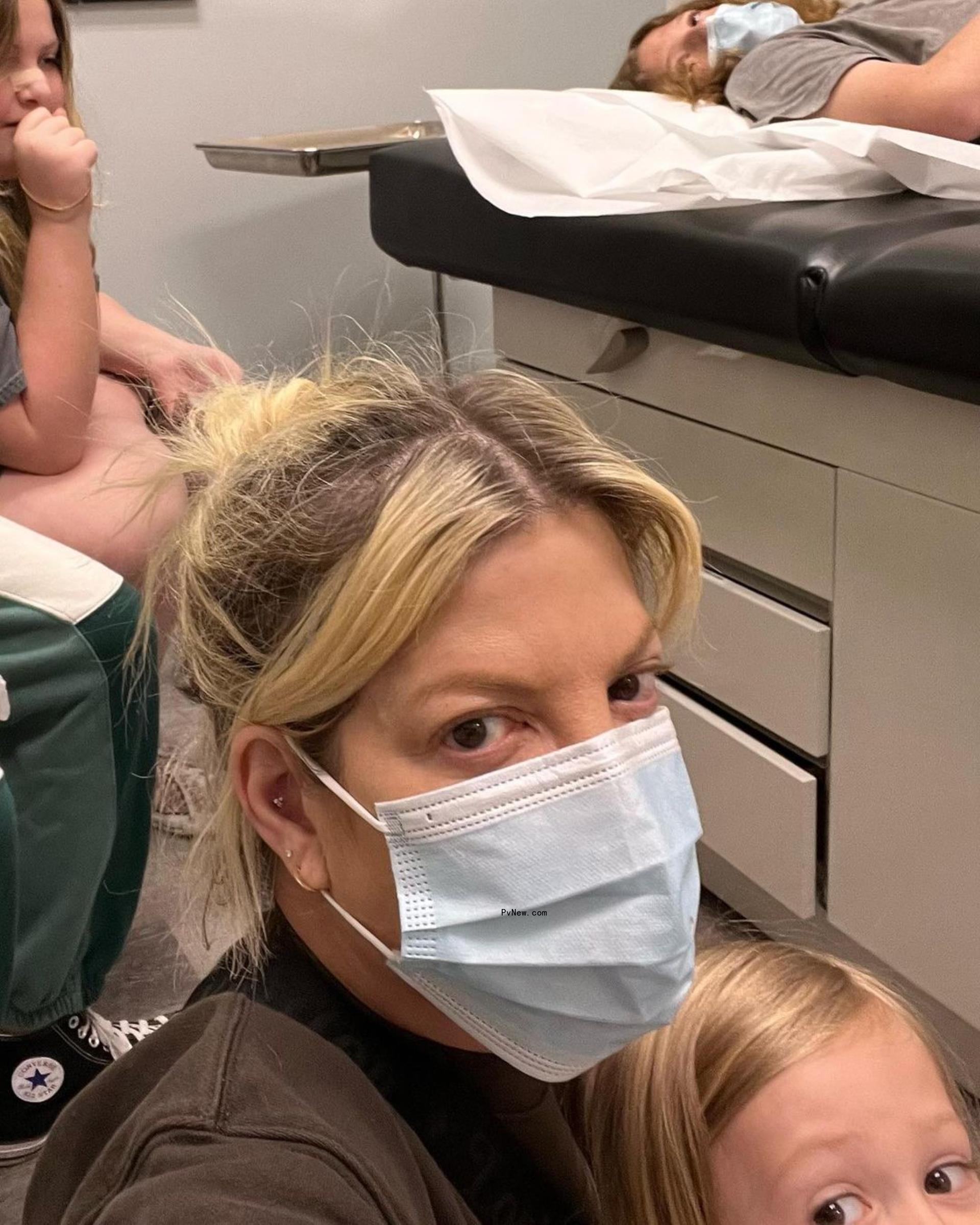 Tori Spelling in a face mask at Urgent Care, while holding one of her kids.