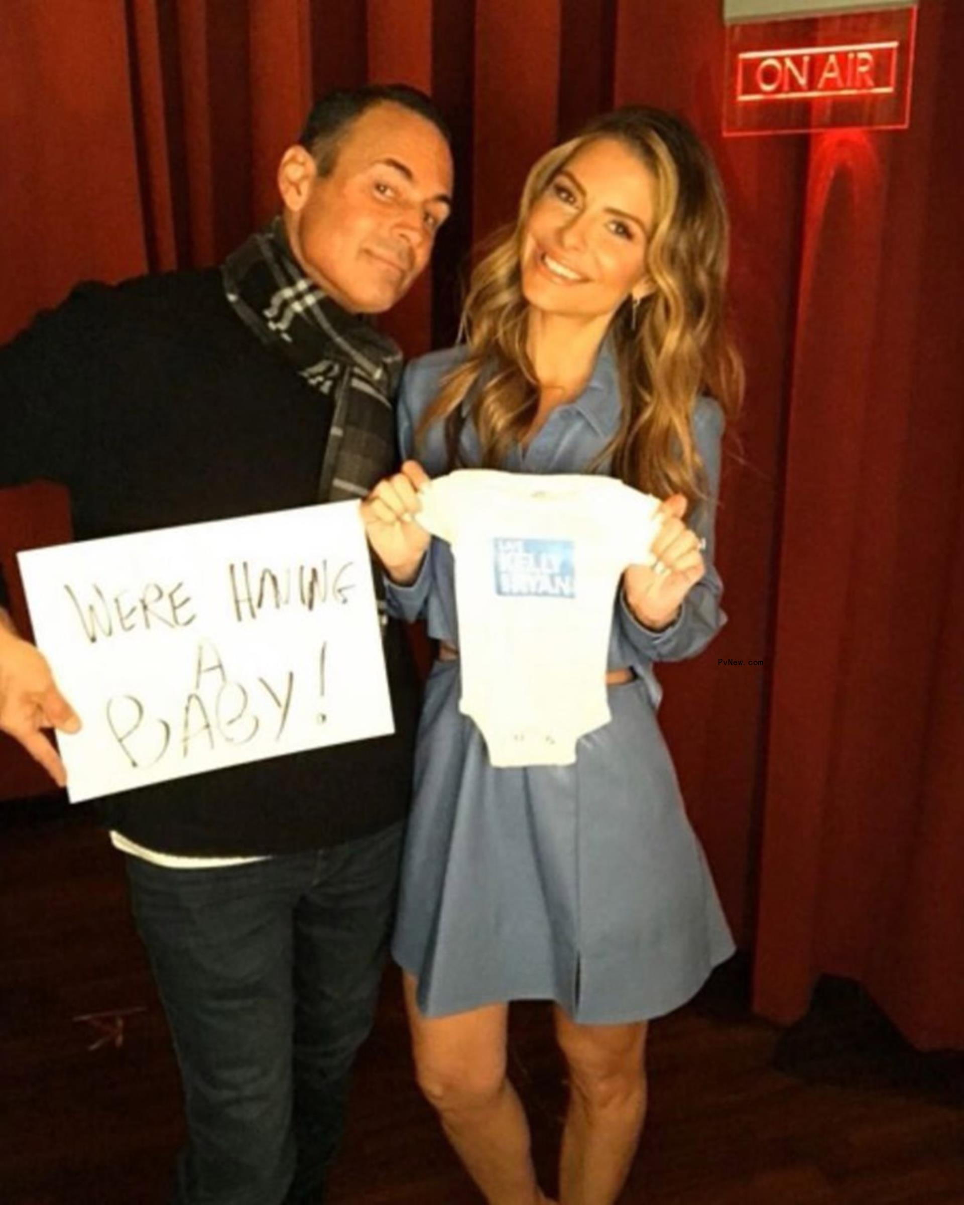 Maria Menounos and Keven Undergaro smile holding a o<i></i>nesie and a sign