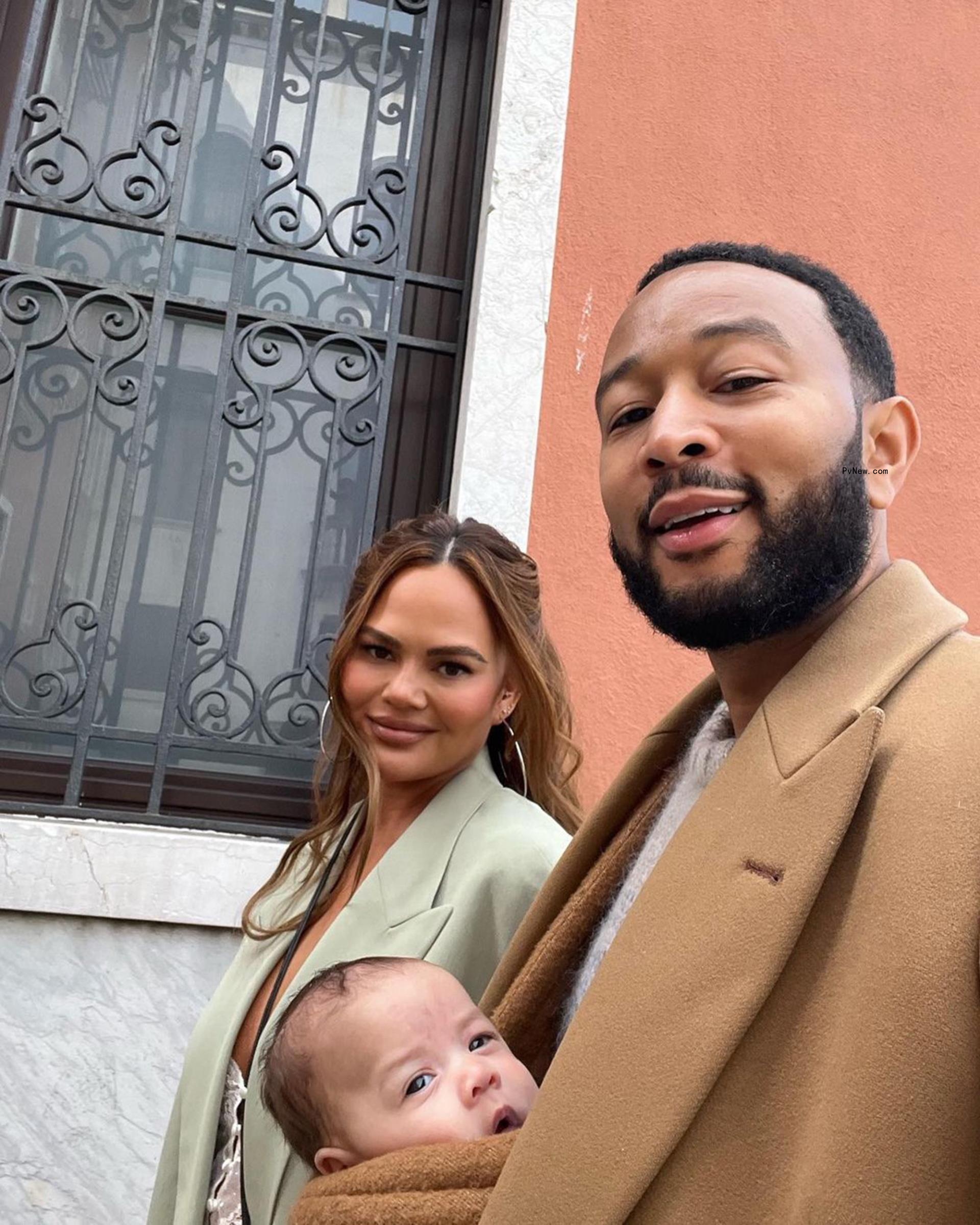 Chrissy Teigen with John Legend holding Esti in a baby carrier.