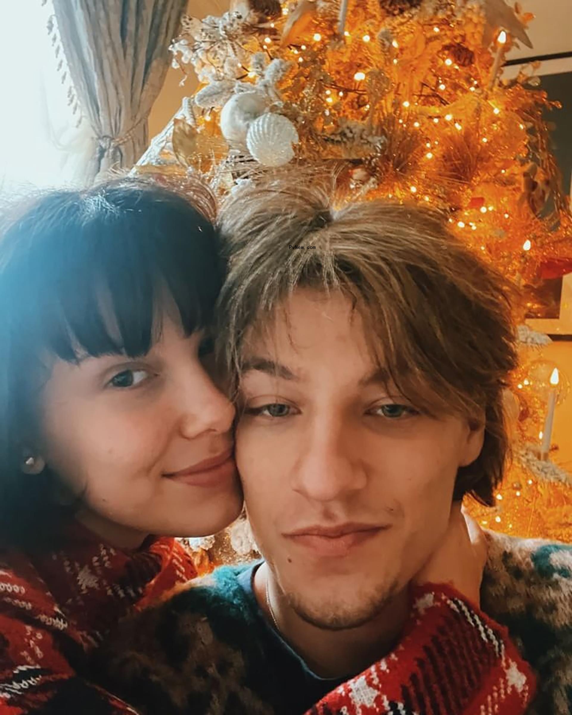 Millie Bobby Brown and Jake Bo<i></i>ngiovi in front of a Christmas tree.