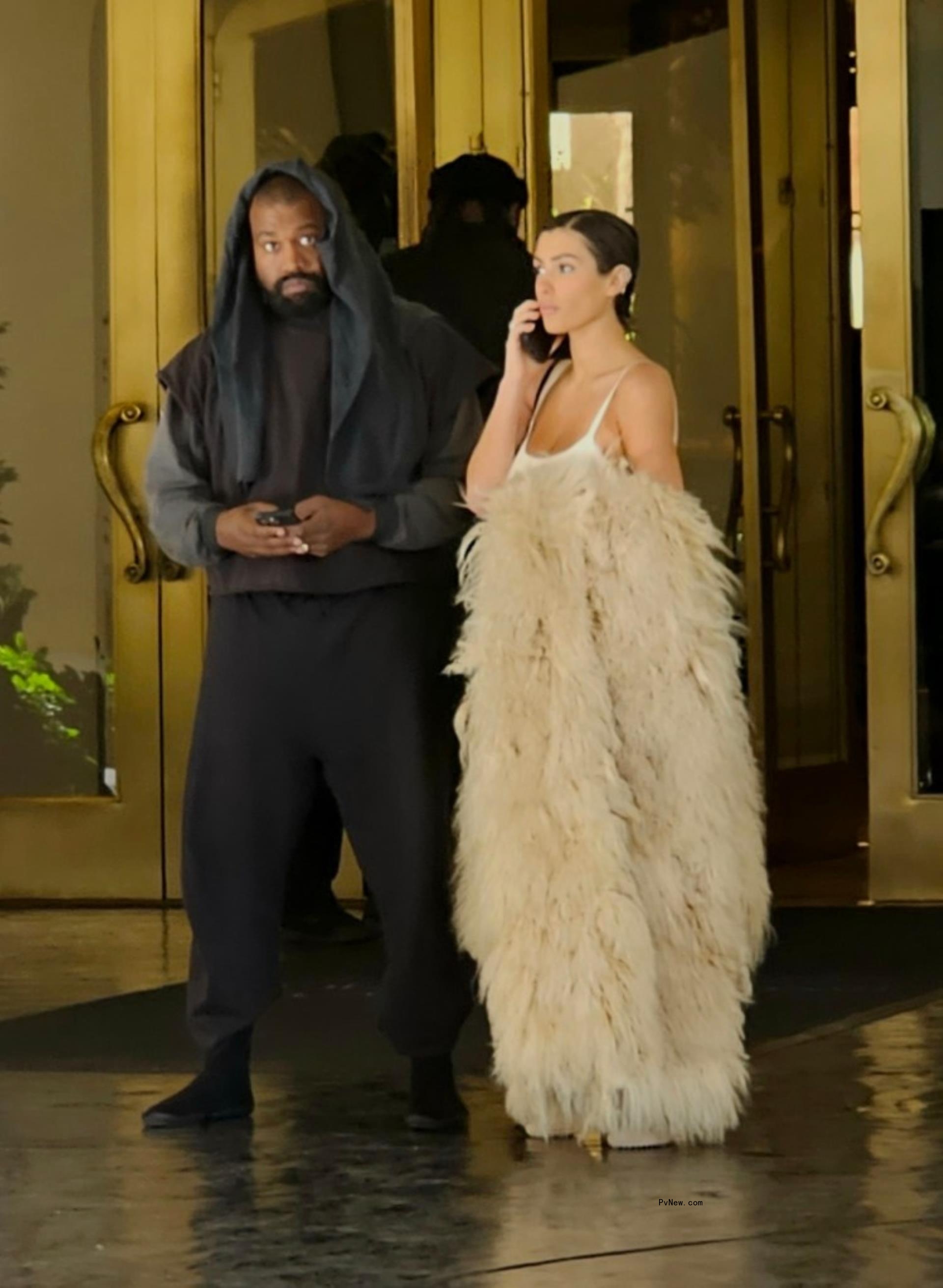 Bianca Censori on her phone standing next to Kanye West