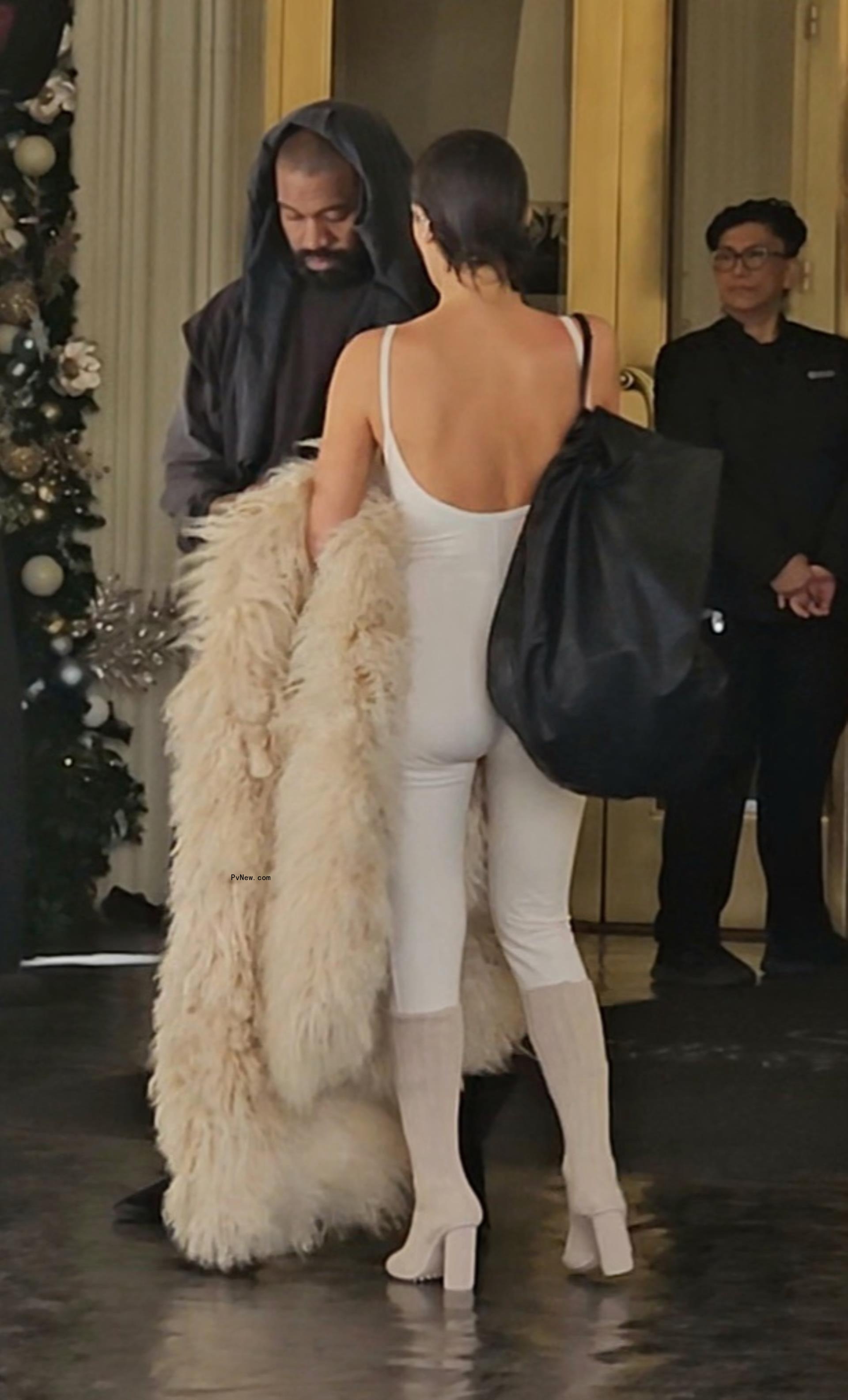 Bianca Censori standing in front of Kanye West who is on his phone