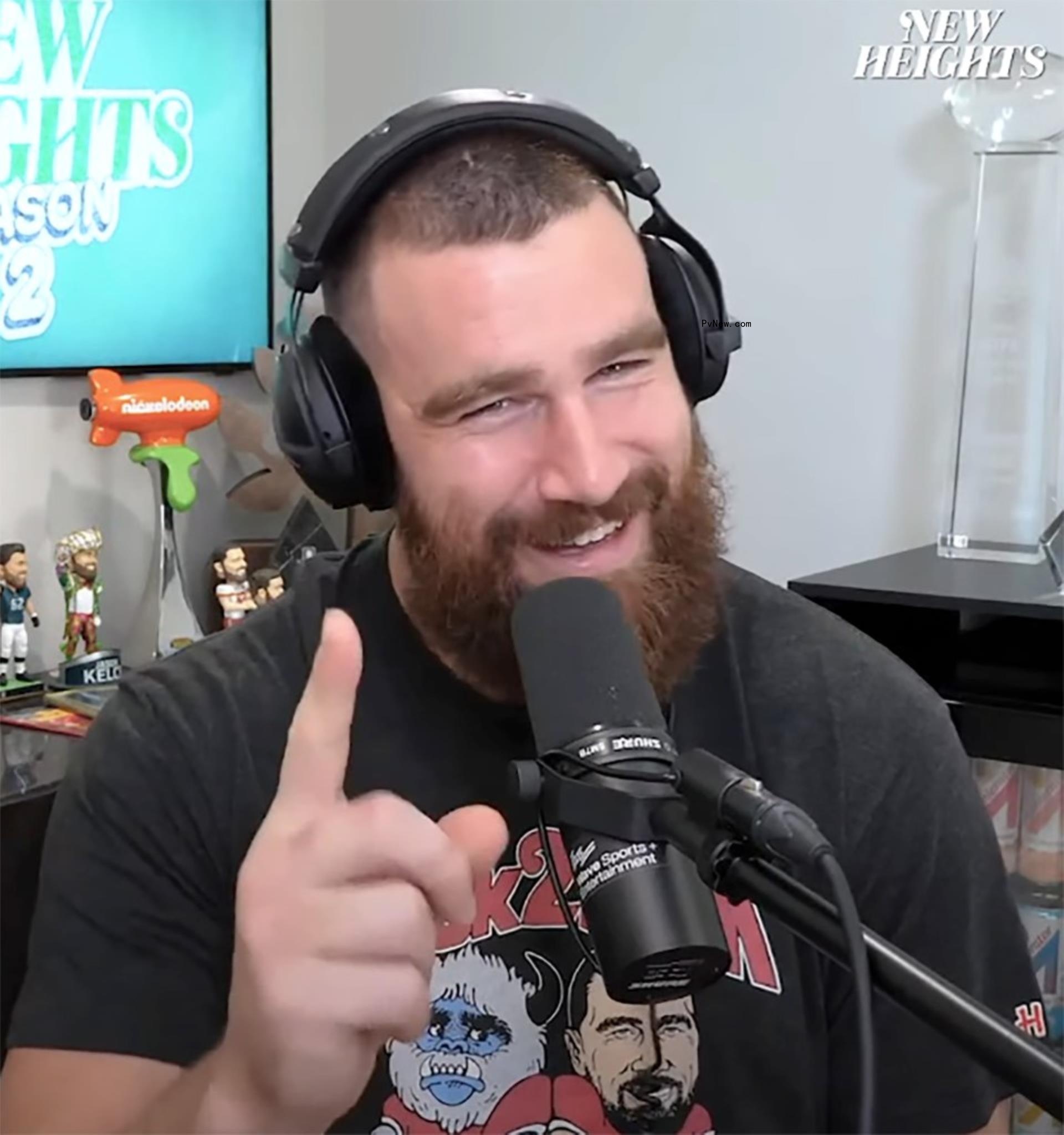 travis kelce talking into a microphone with his finger up