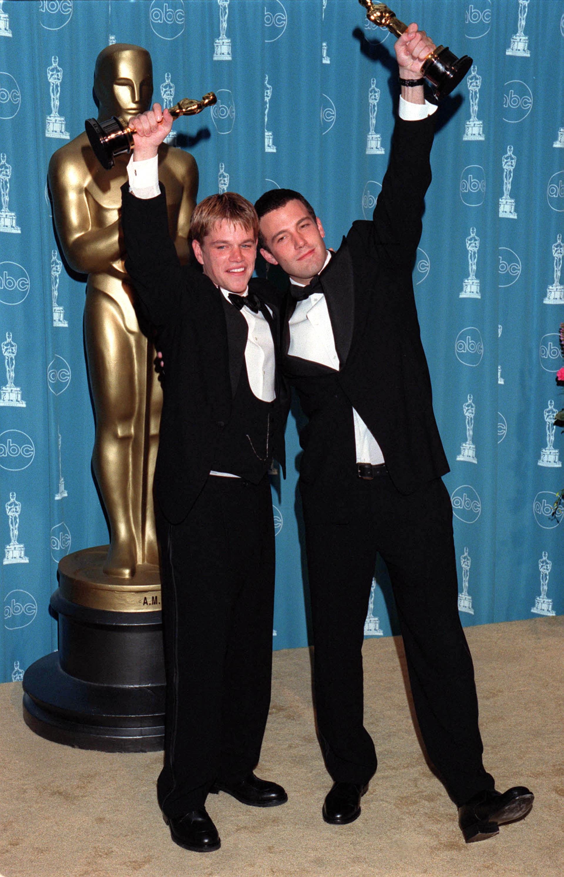 Matt Damon and Ben Affleck holding up their awards at the Oscars.