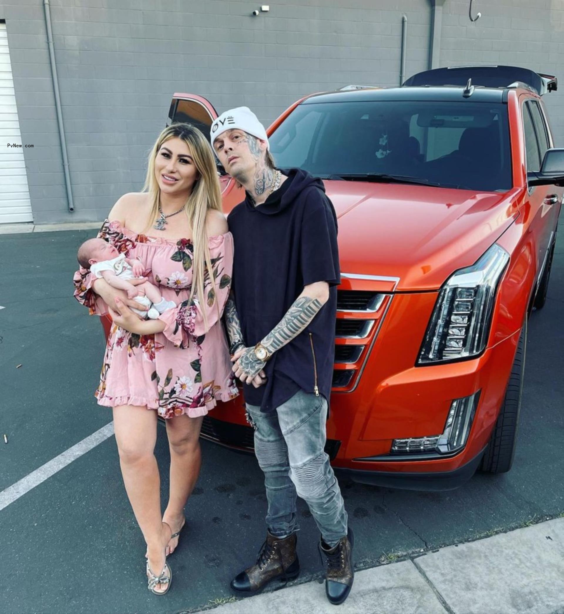 Aaron Carter posing in front of a car with Melanie Martin and their child.