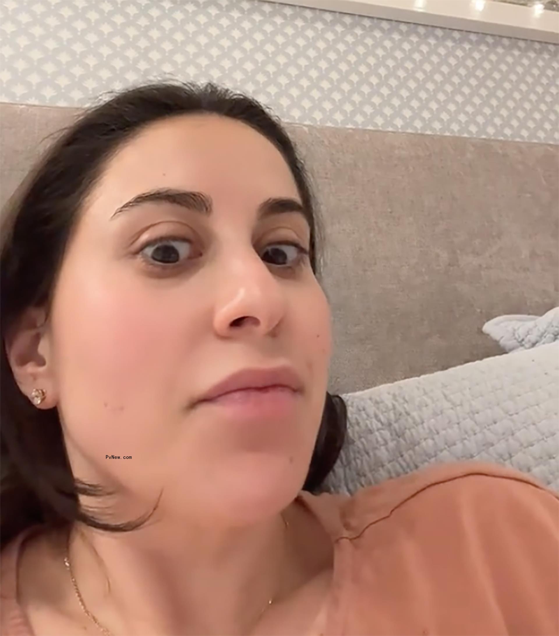 A still of Claudia Oshry's face from a TikTok video she posted. She is wearing an orange shirt and is in bed.