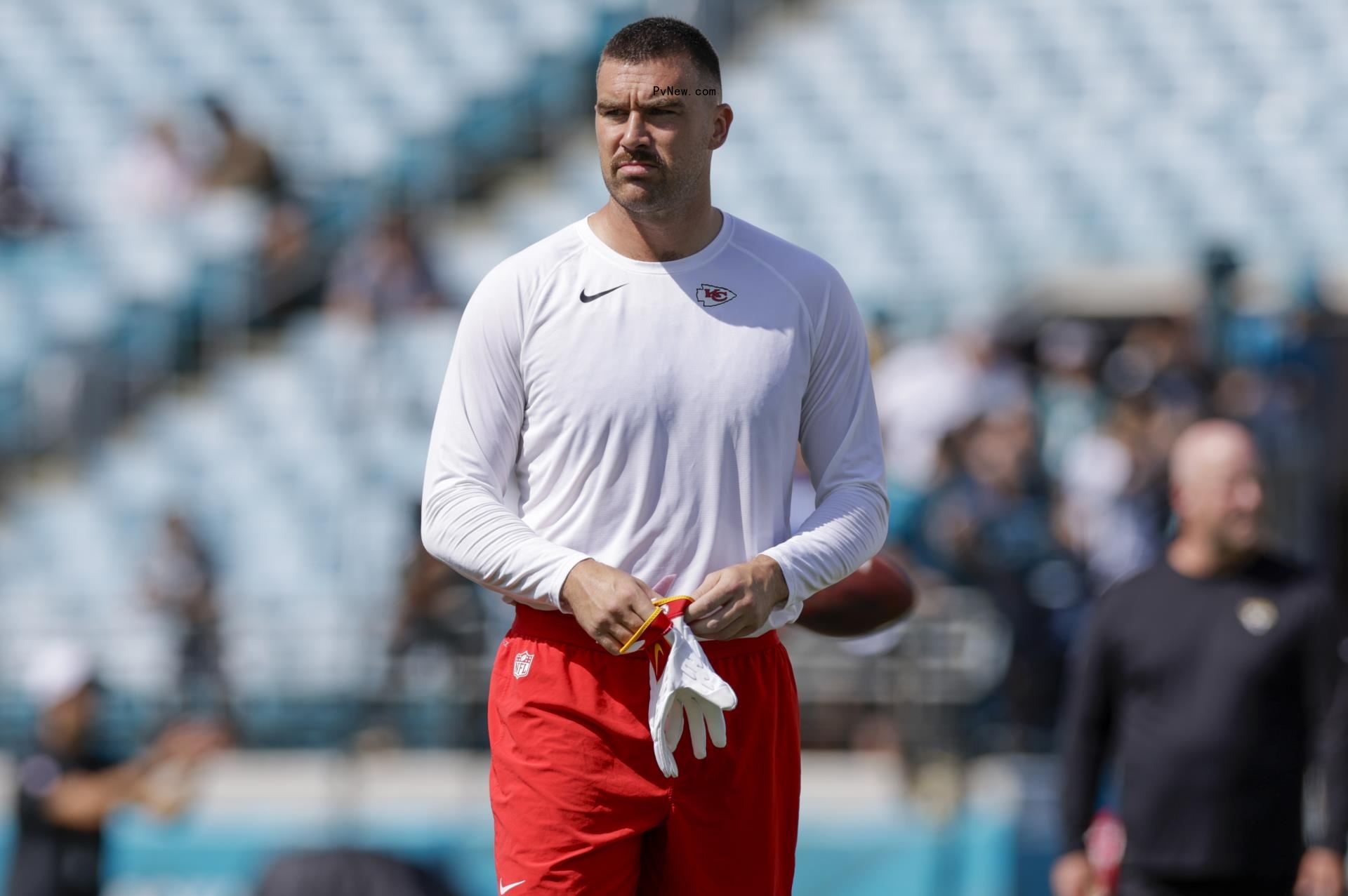 Travis Kelce on football field in red shorts and a white Nike tee