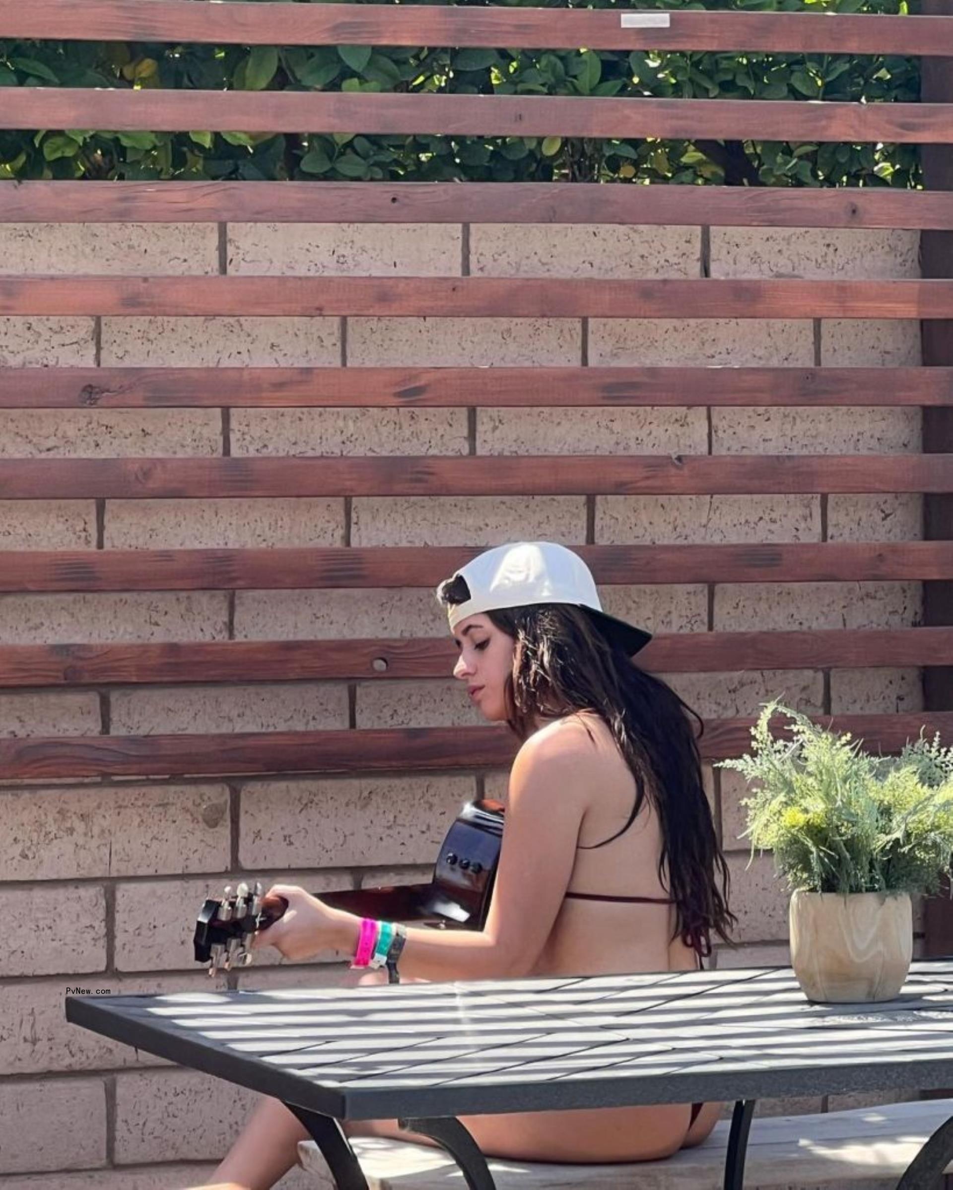 Camila Cabello playing a guitar outdoors.