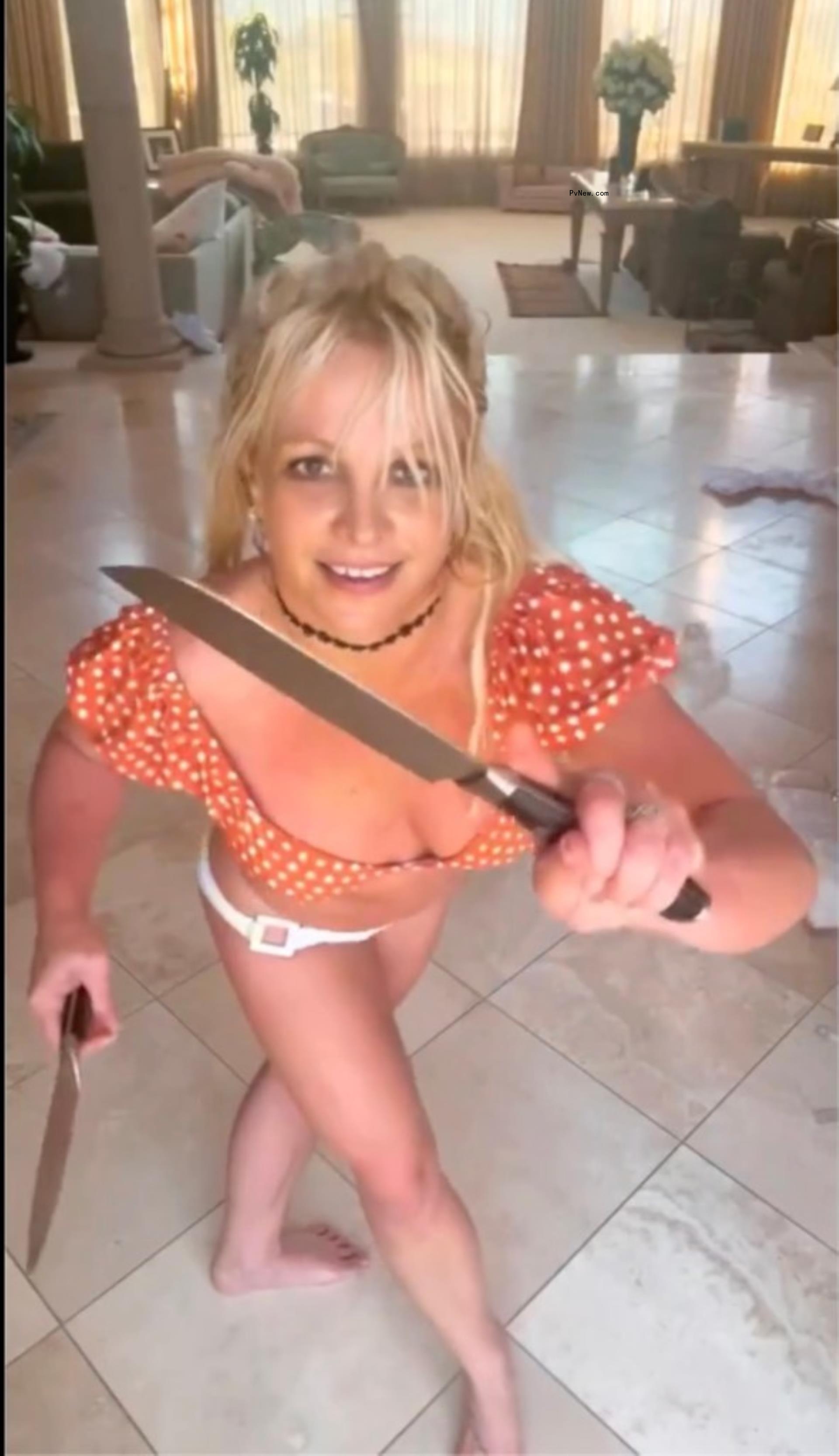 Britney Spears in an orange crop top and white bikini bottoms dancing with knives.