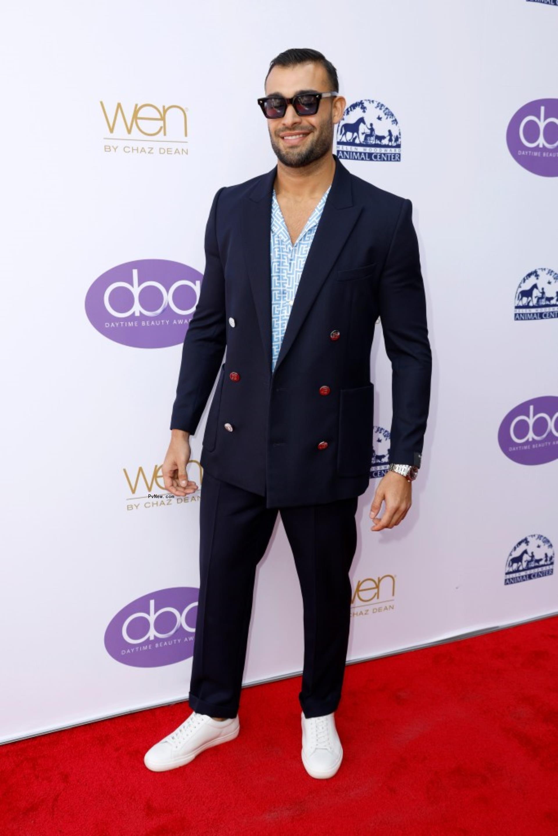 Sam Asghari in a navy blue suit on a red carpet.