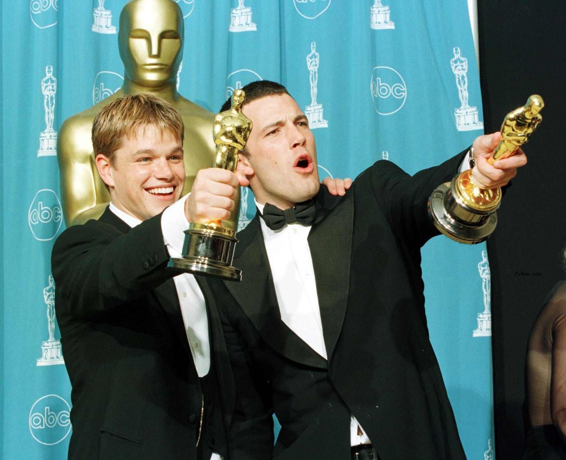 Matt Damon and Ben Affleck at the Oscars cheering and celebrating while holding the awards.