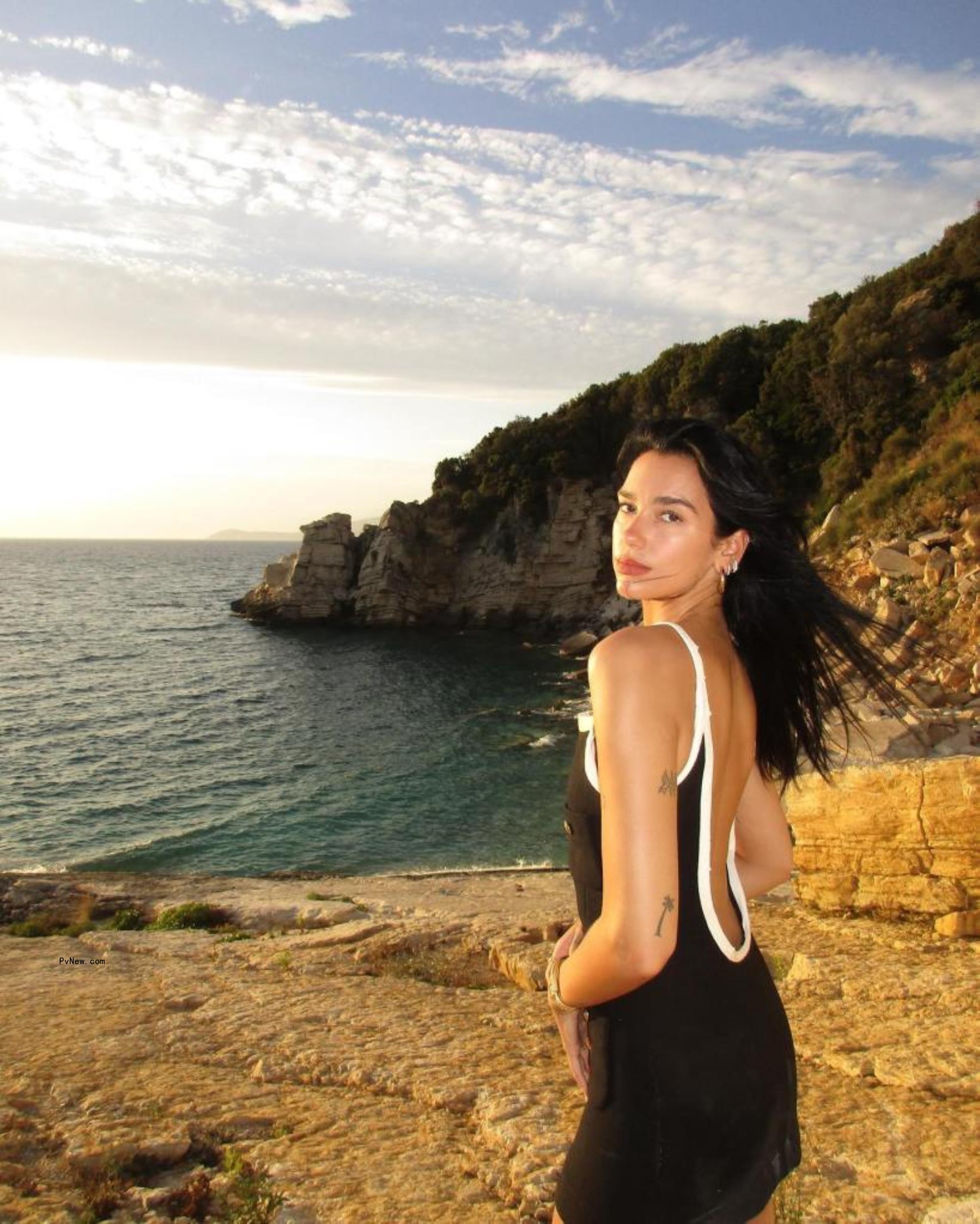 Selena Gomez in front of a pool and palm trees posing in a polka dot and butterfly print dress while leaning on a matching trunk