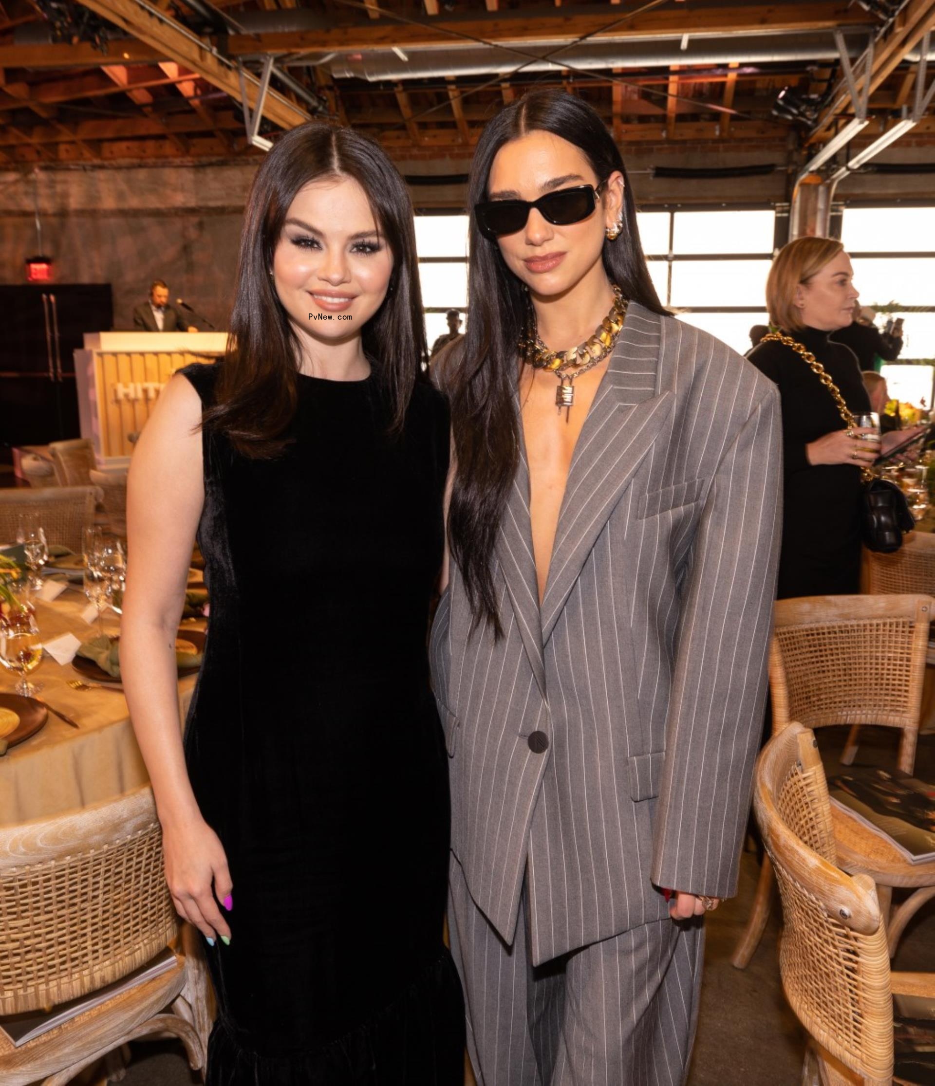 Selena Gomez in a black dress posing with Dua Lipa in a gray suit