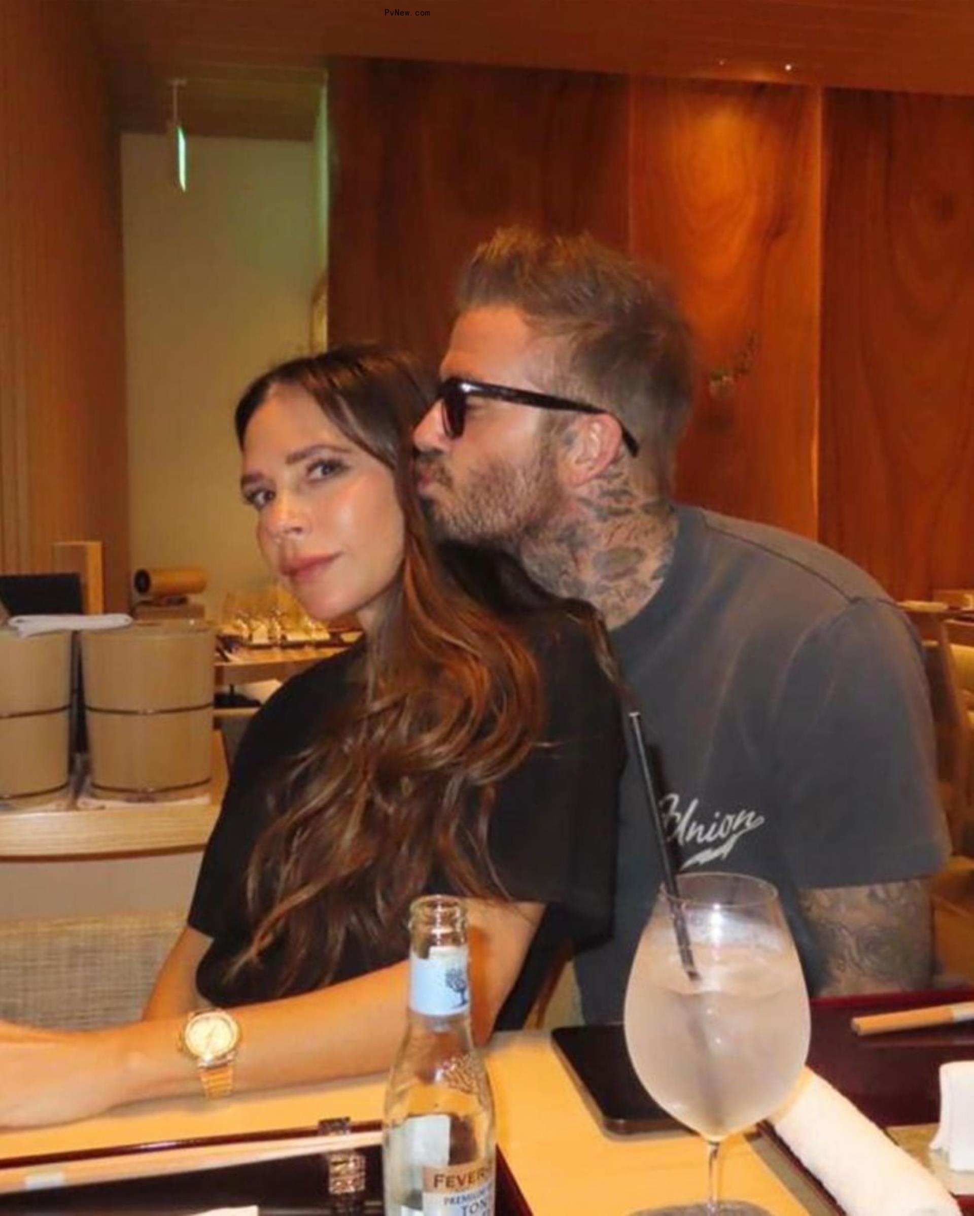 David Beckham kissing wife Victoria on the cheek at a table. 
