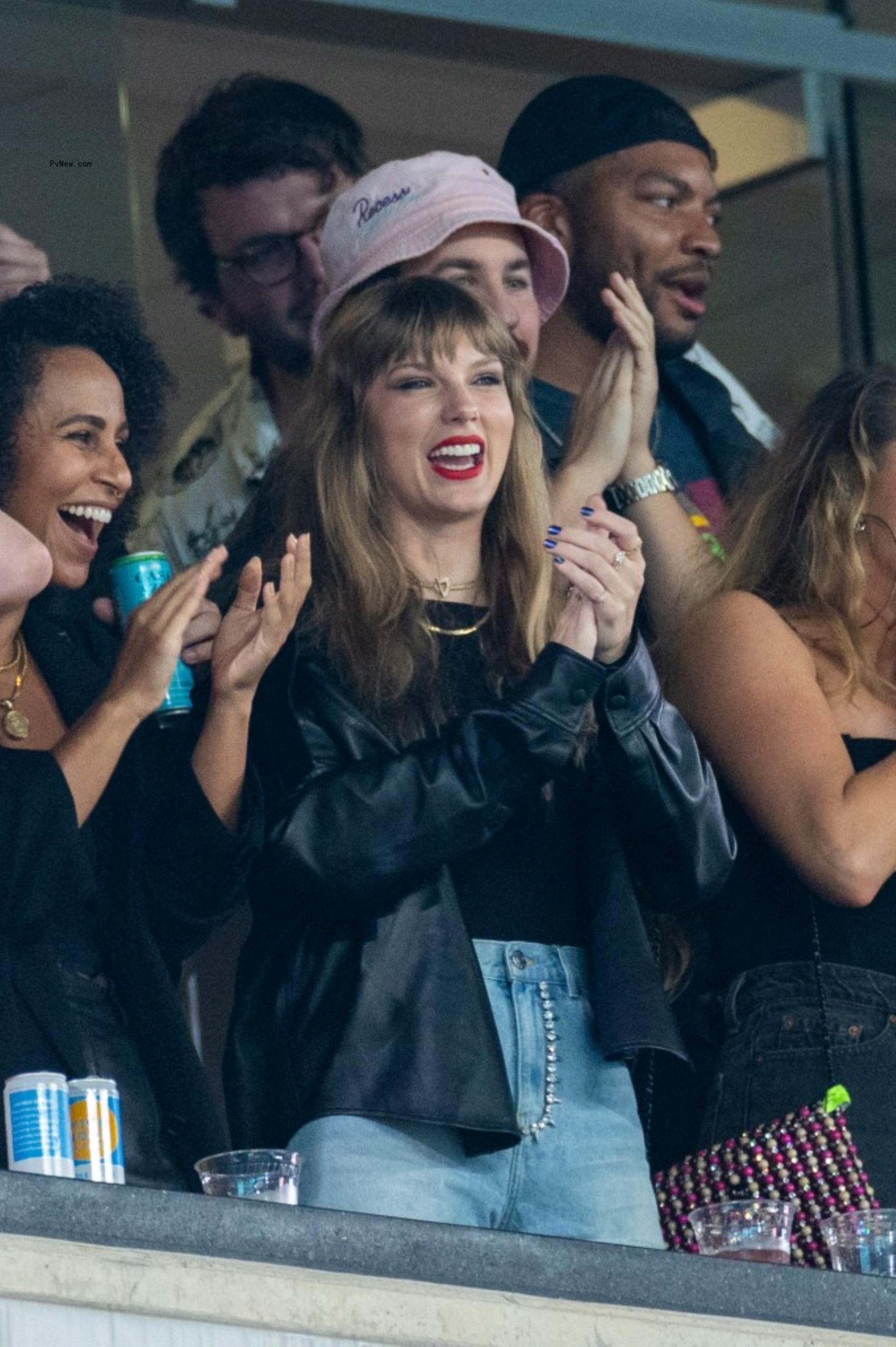 Taylor Swift in black shirt and jean shorts cheering from a VIP booth at a football game