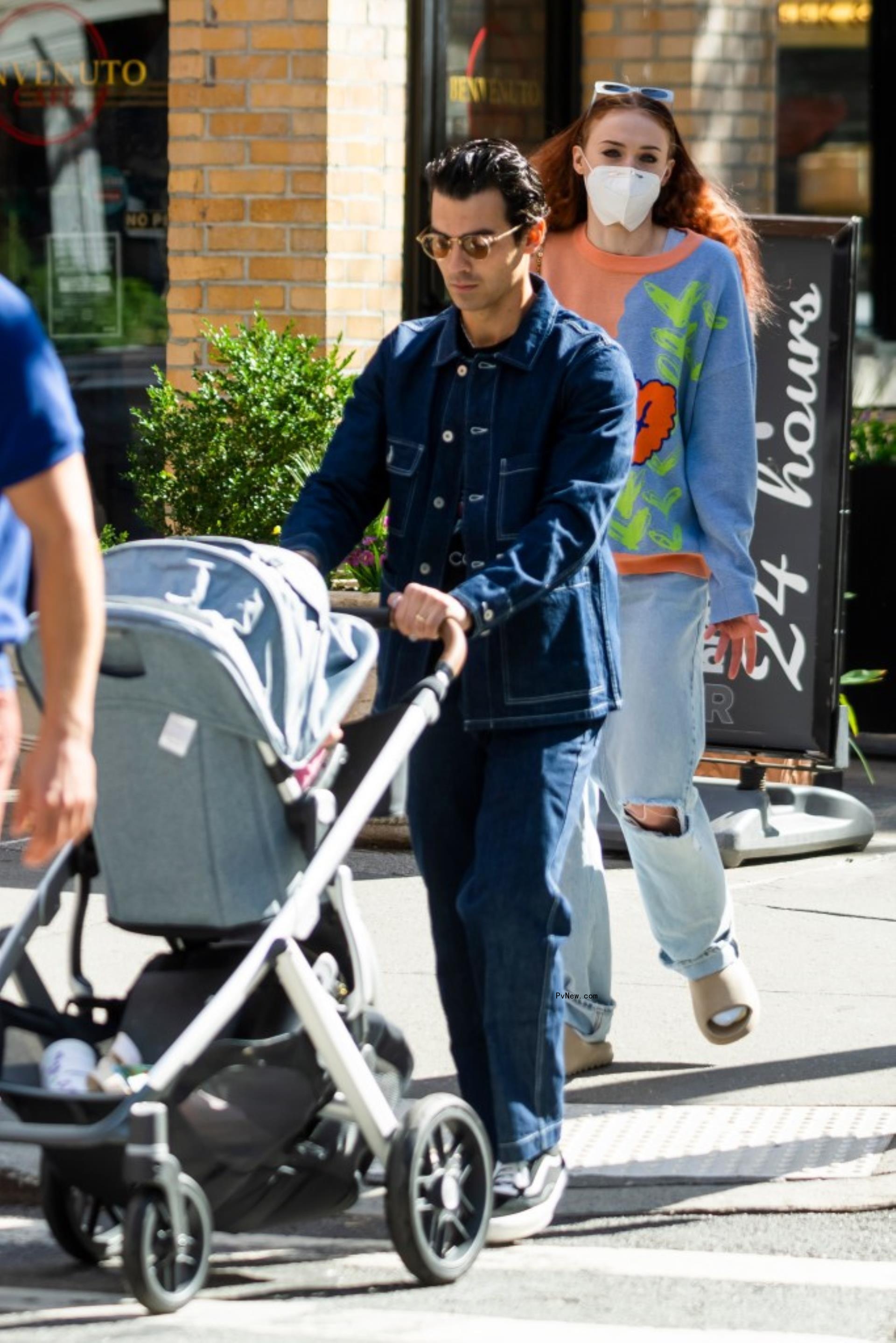 Joe Jo<i></i>nas pushing a stroller as Sophie Turner walks behind him.