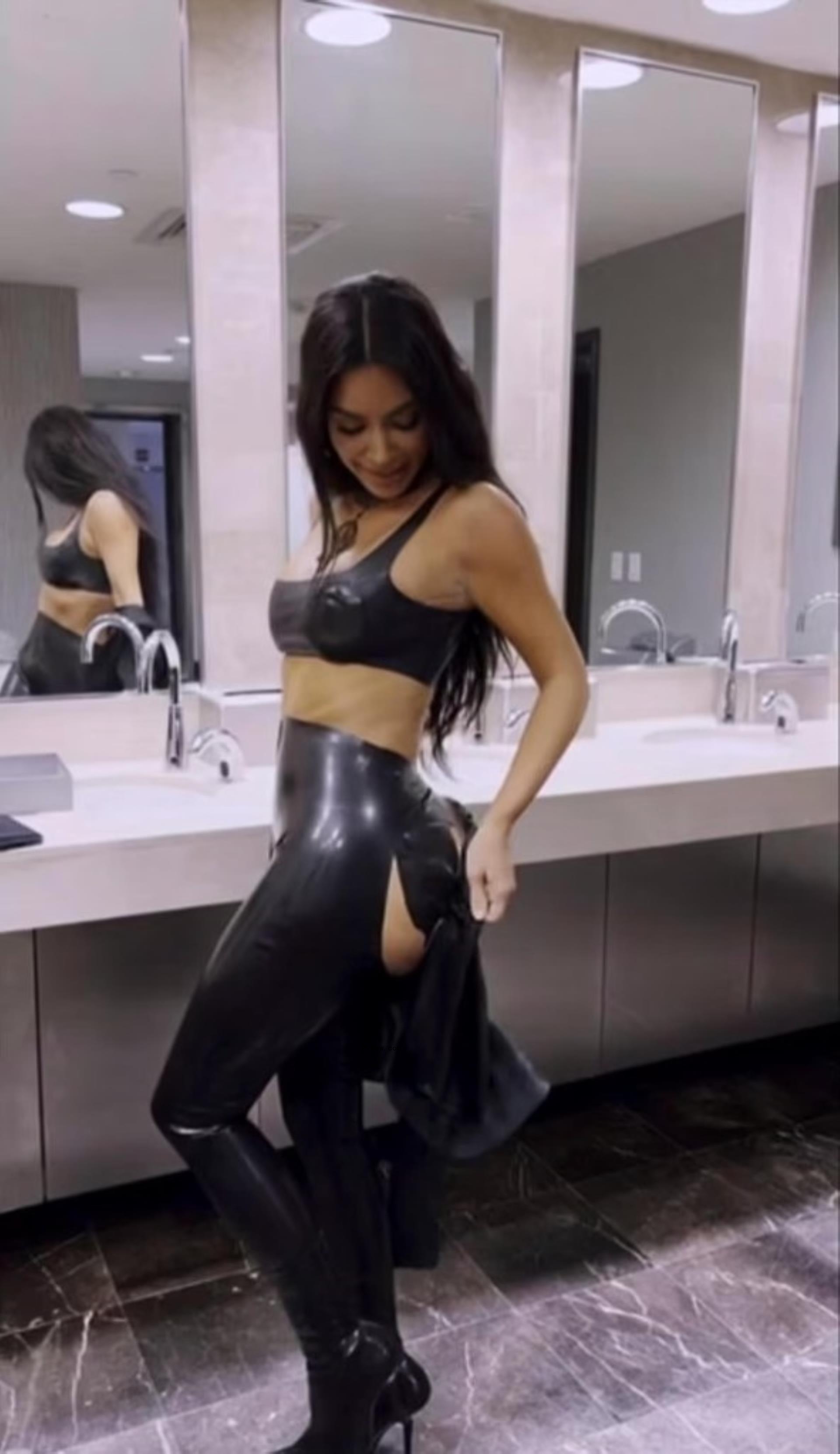 Kim Kardashian looking at her black latex leggings as they were shredded at her butt