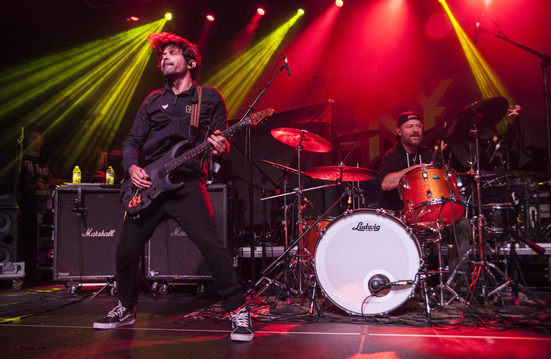 Jess Margera playing the drums while his band member plays the guitar.