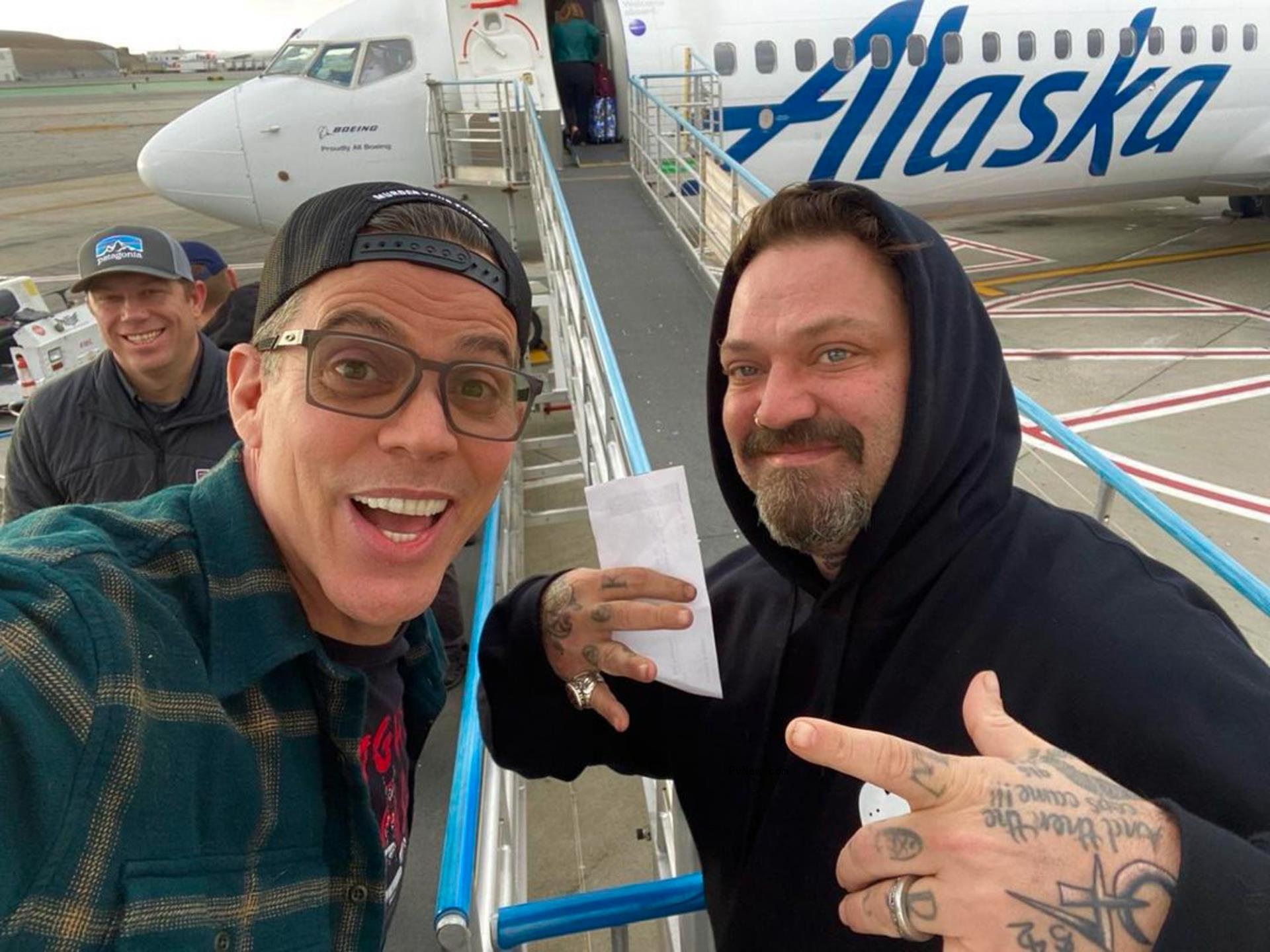 Bam Margera posing for a picture with Steve-O in front of a plane.