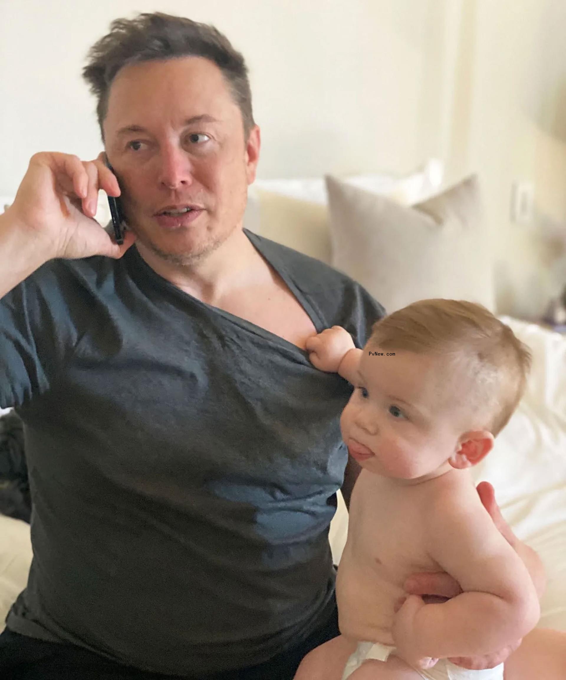 Elon Musk with a baby pulling on his shirt.