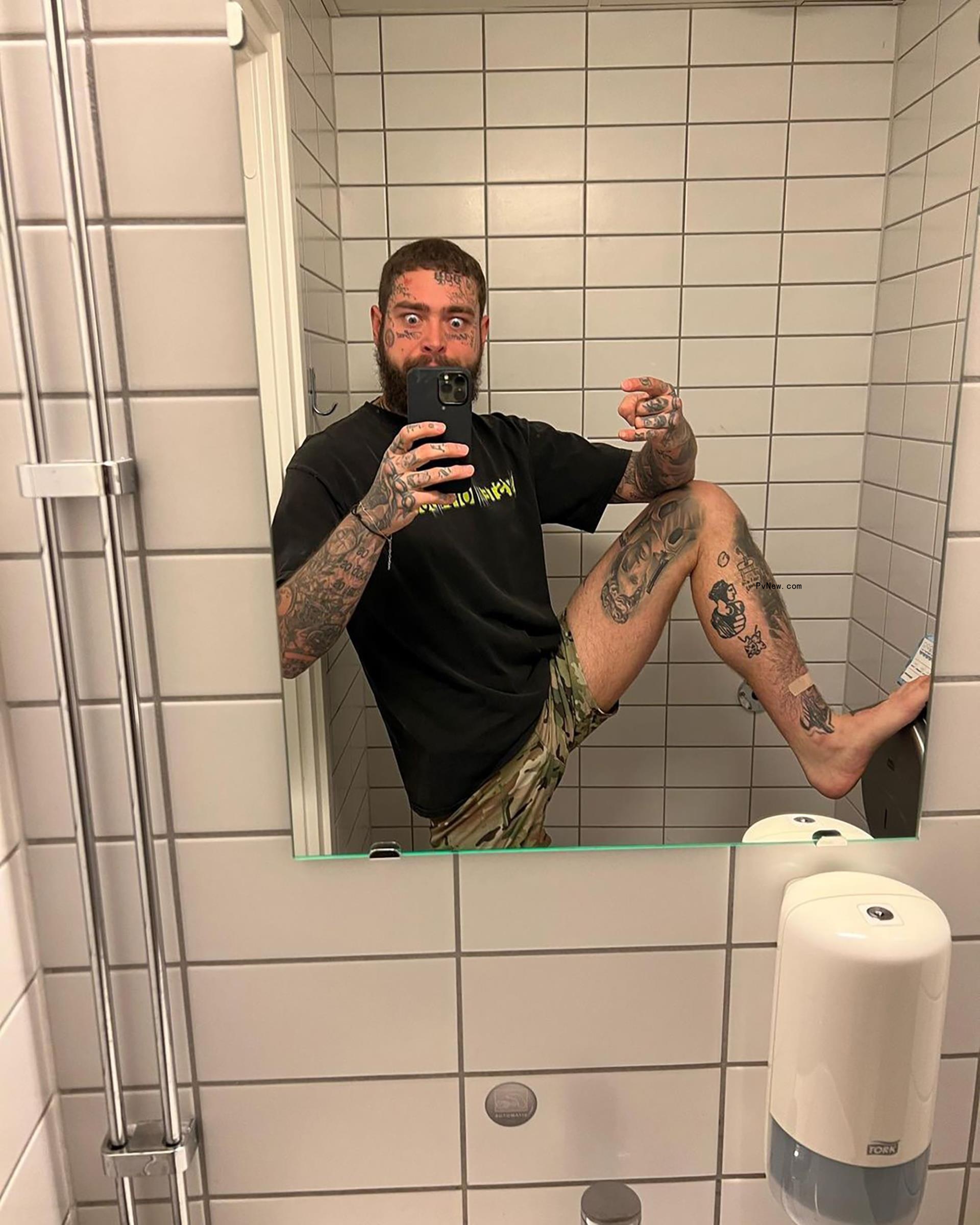 Post Malone taking a mirror selfie wearing o<i></i>nly a T-shirt and propping his leg up on the wall.