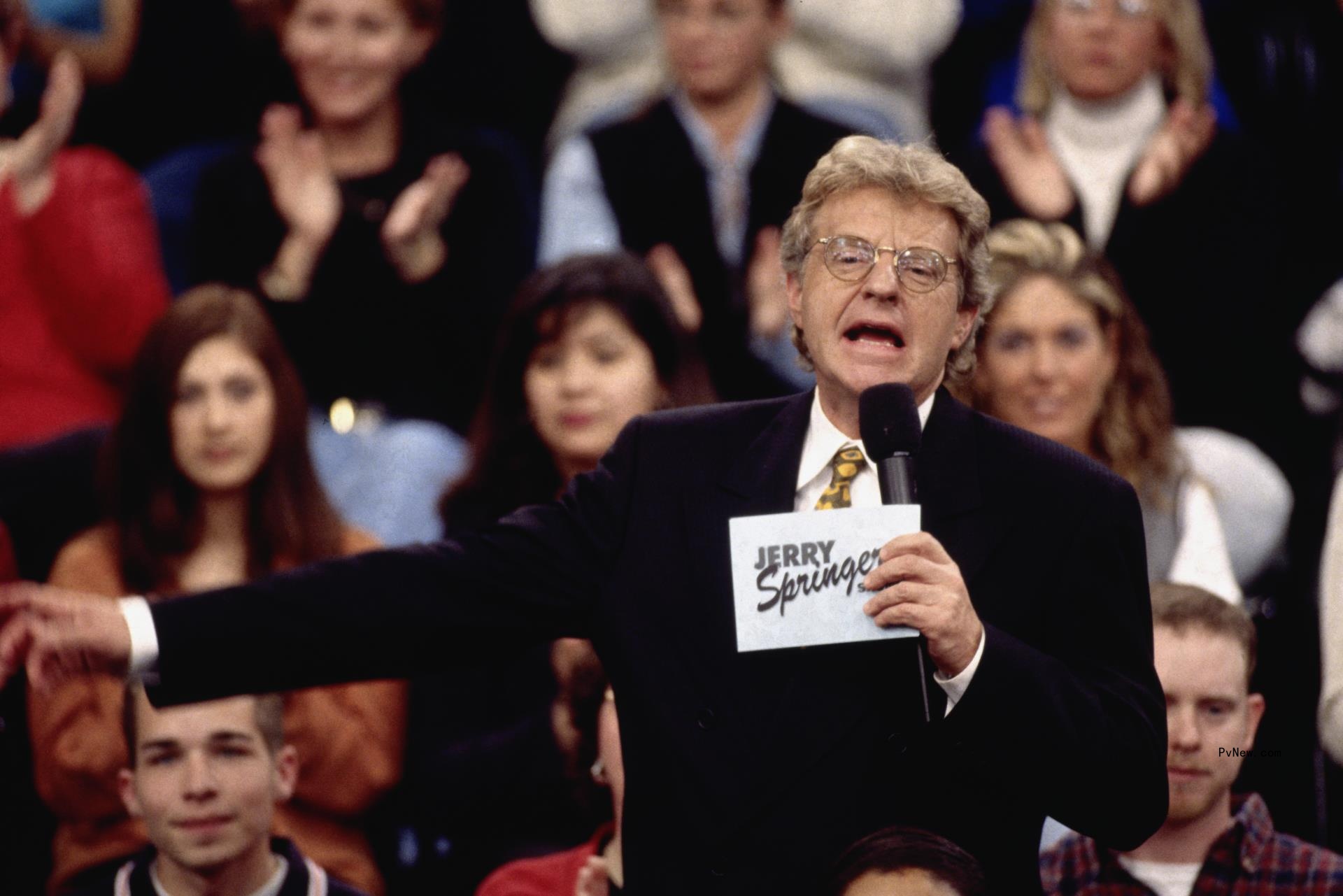 Jerry Springer speaks into mic in front of audience