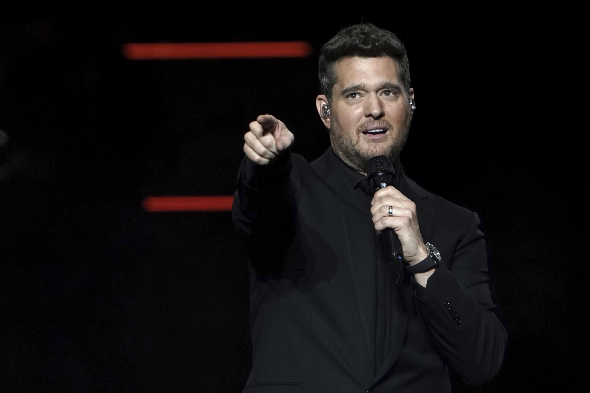 Michael Bublé pointing his finger while holding a mic with his other hand onstage.