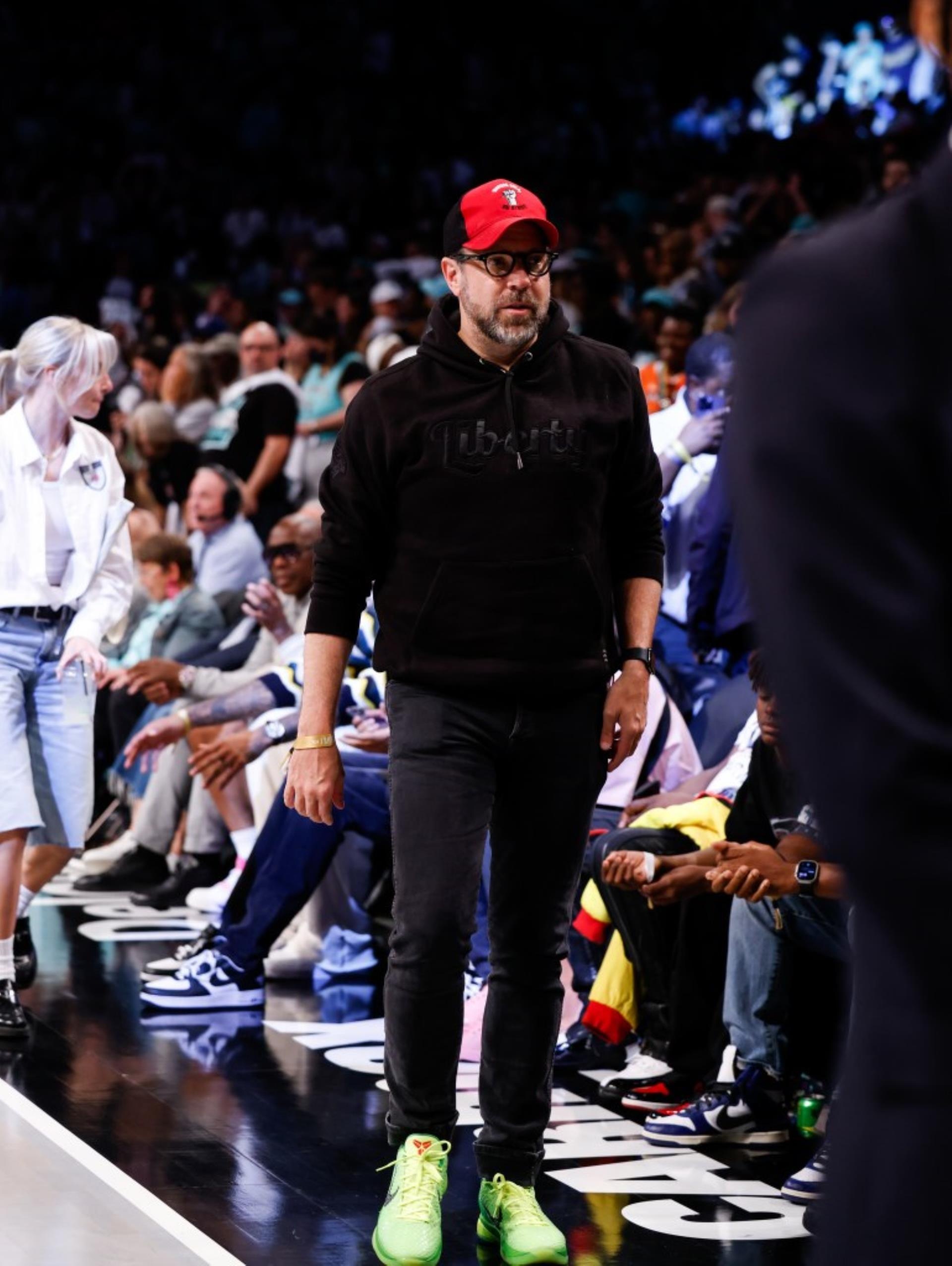 Jason Sudeikis  in an all black outfit walking courtside at a basketball game