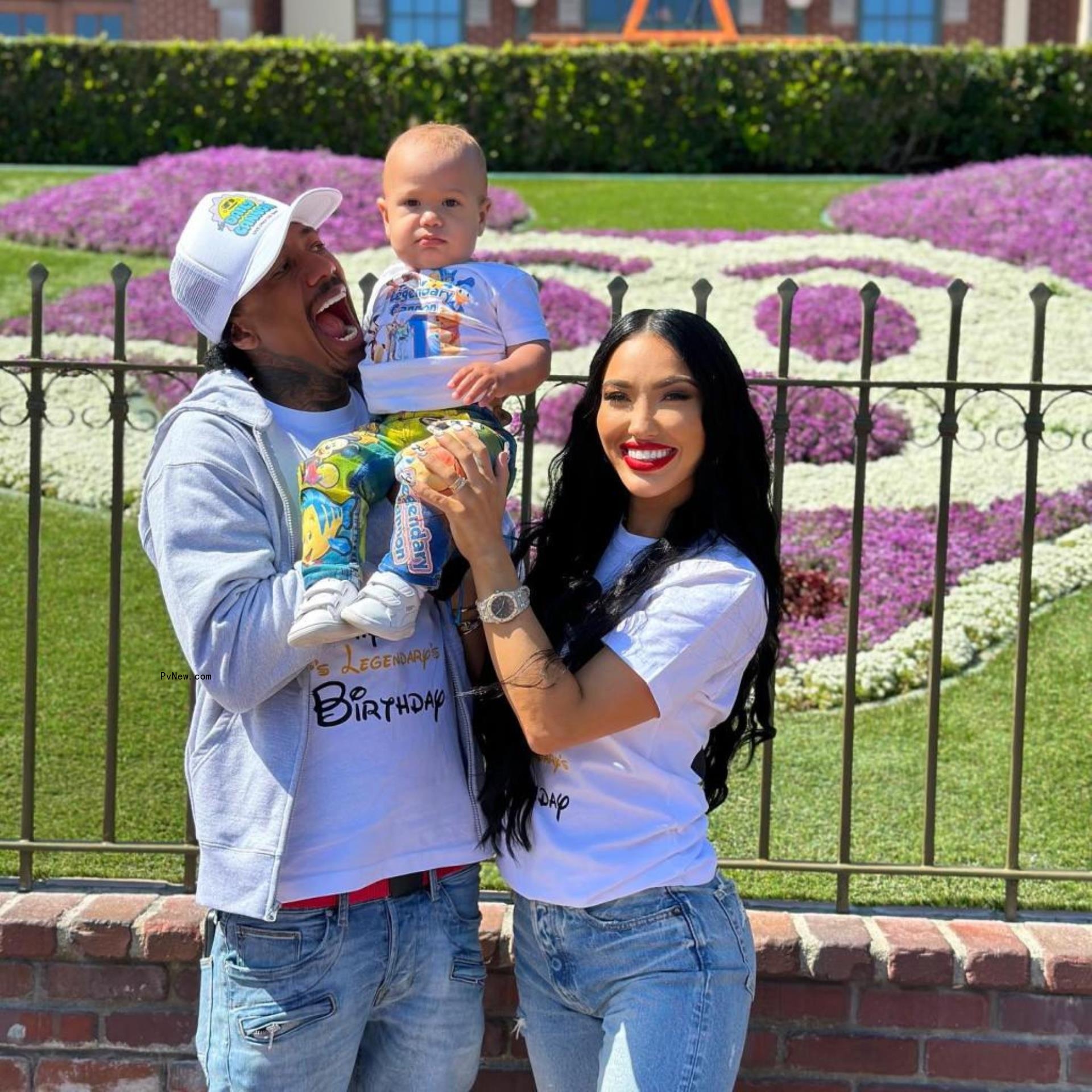 Nick Cannon and Bre Tiesi smile with their child at Disneyland in front of flower shaped like Mickey's head