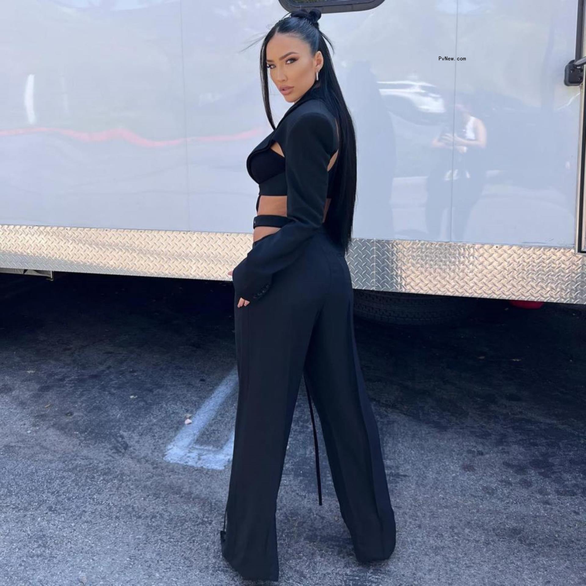 Bre Tiesi poses with her back to the camera in a black crop top and black trousers