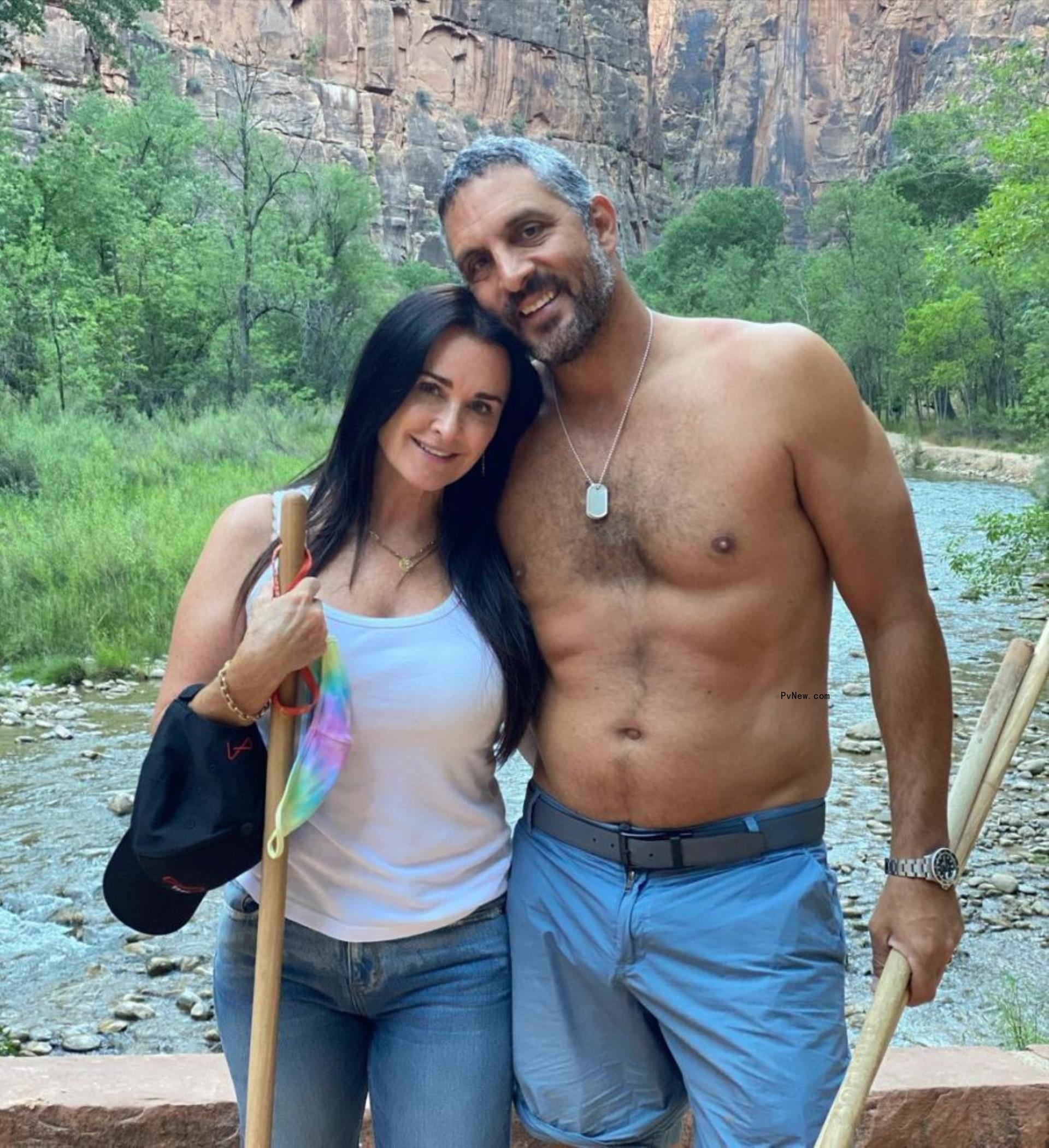 Kyle Richards and Mauricio Umansky smile outdoors. Richards is in jeans and a white tank and Umansky is shirtless and in blue shorts.