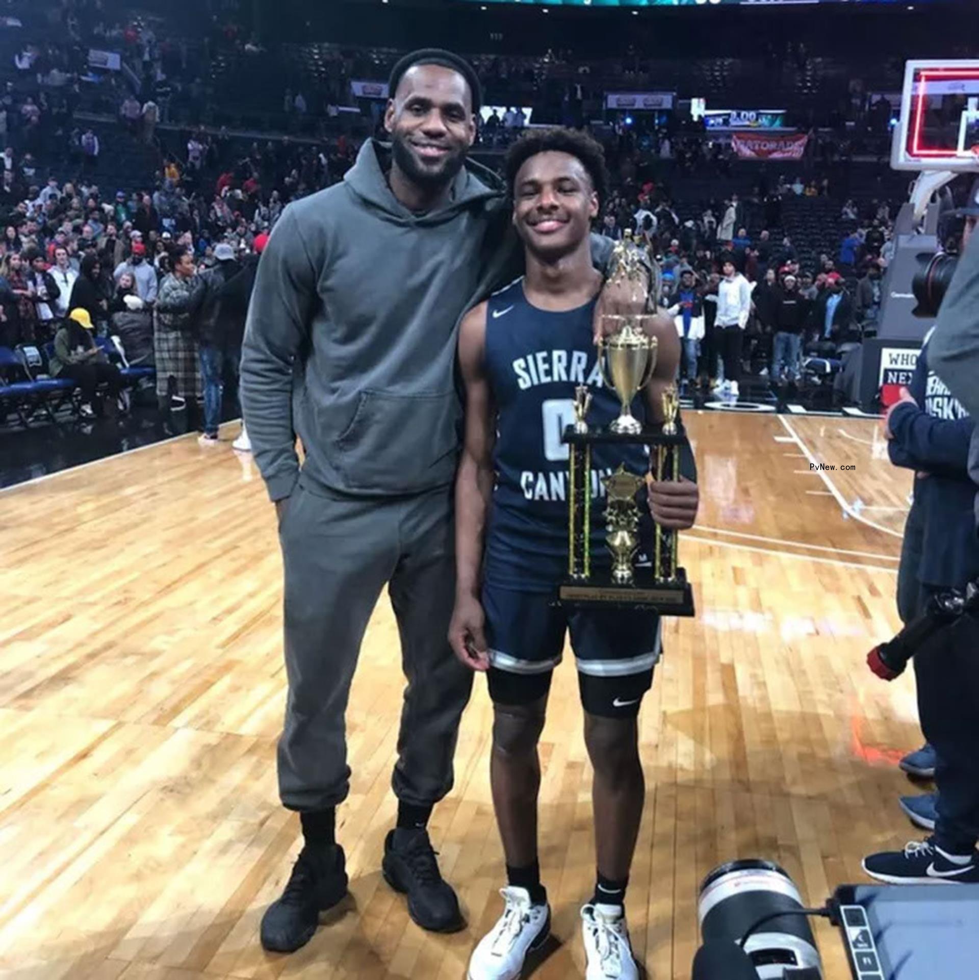 lebron james with his arm wrapped around his son bro<i></i>nny who is holding a trophy