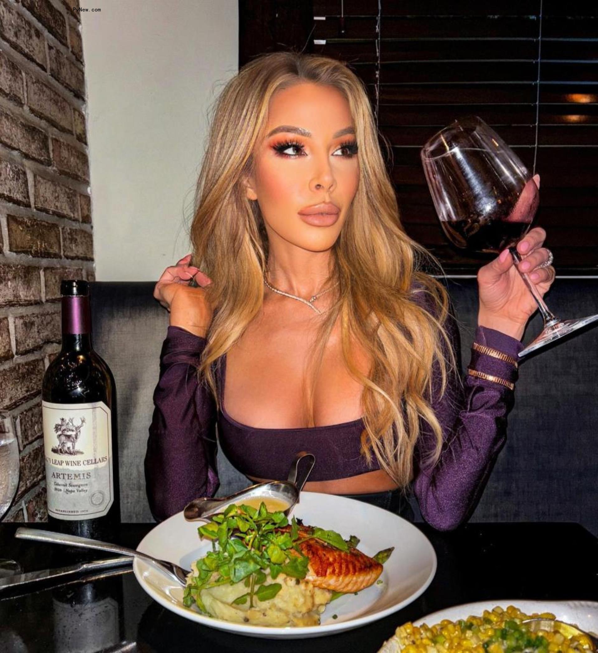 lisa hochstein holding a glass of wine at a restaurant table with fish in front of her