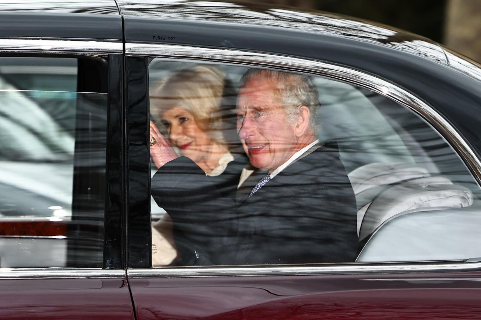 King Charles and Queen Camilla wave to crowds from their car.