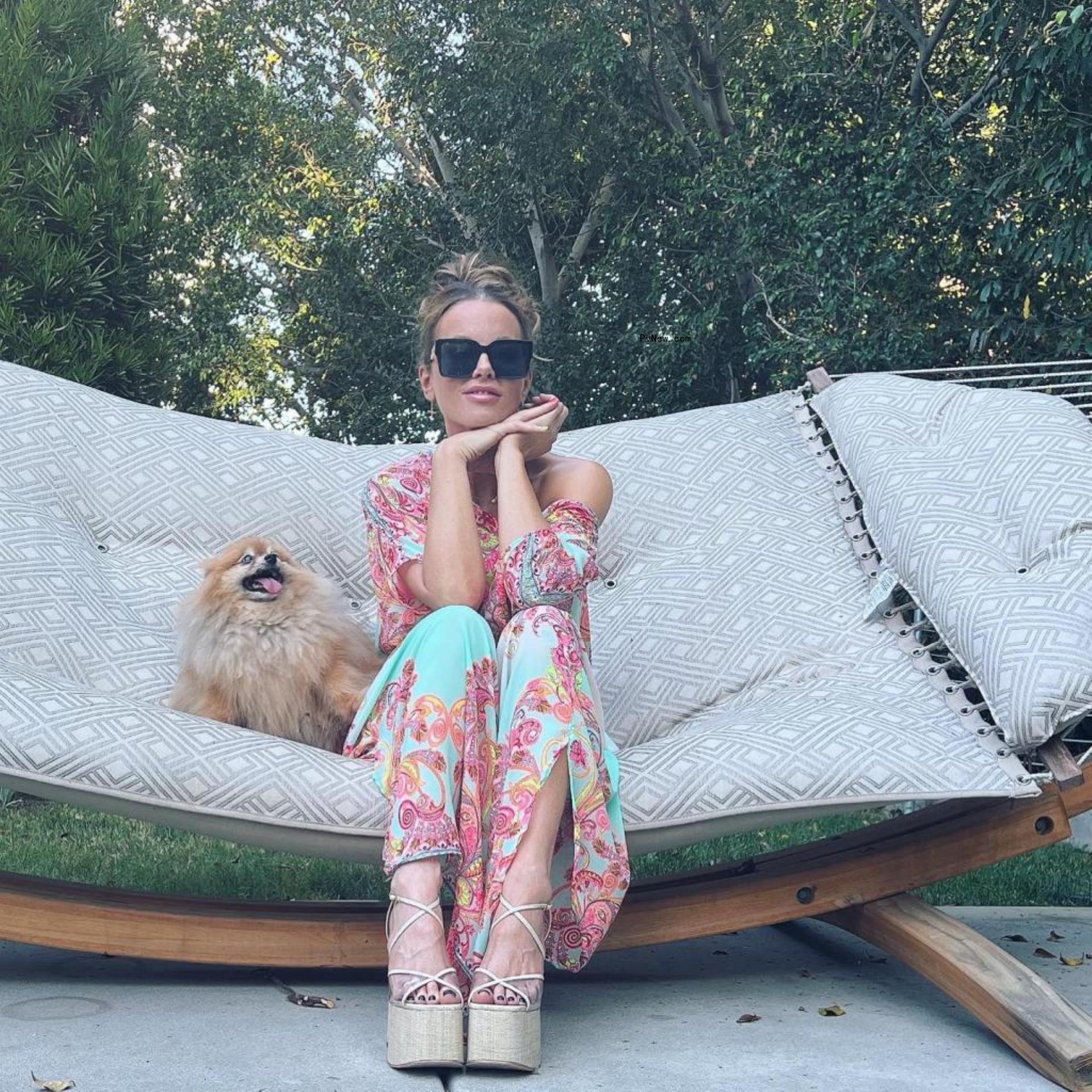Kate Beckinsale sitting in long dress on hammock with dog.