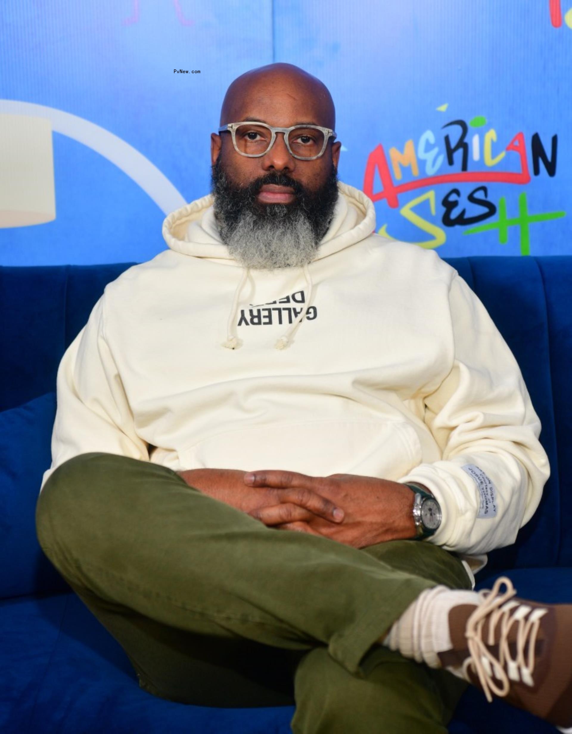 Richelieu Dennis sitting with legs crossed on stage.