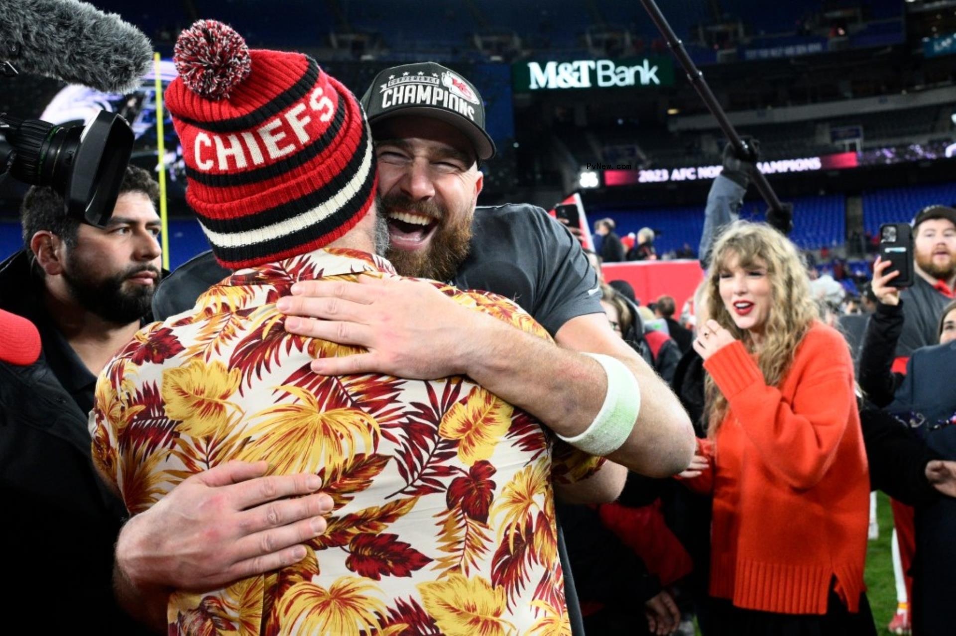 Jason and Travis Kelce hugging with Taylor Swift in the background.