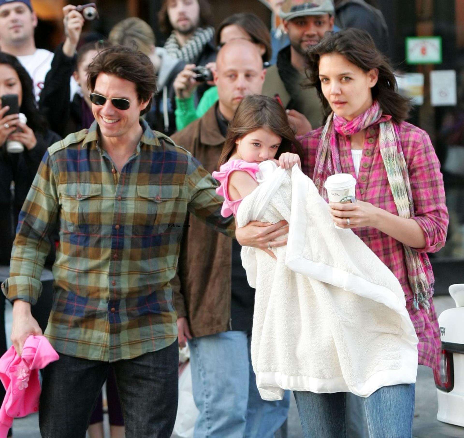 Katie Holmes carries Suri Cruise as Tom Cruise walks beside them.