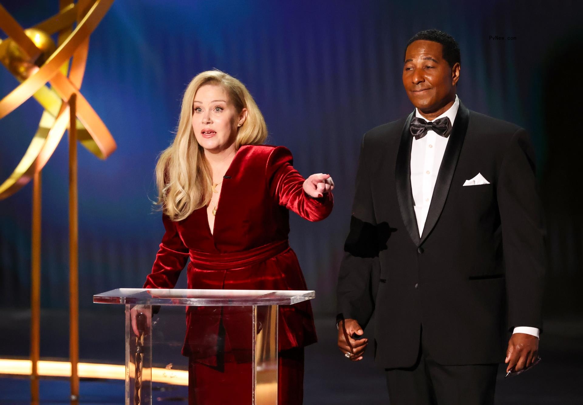 christina applegate standing at a podium and pointing at the man next to her