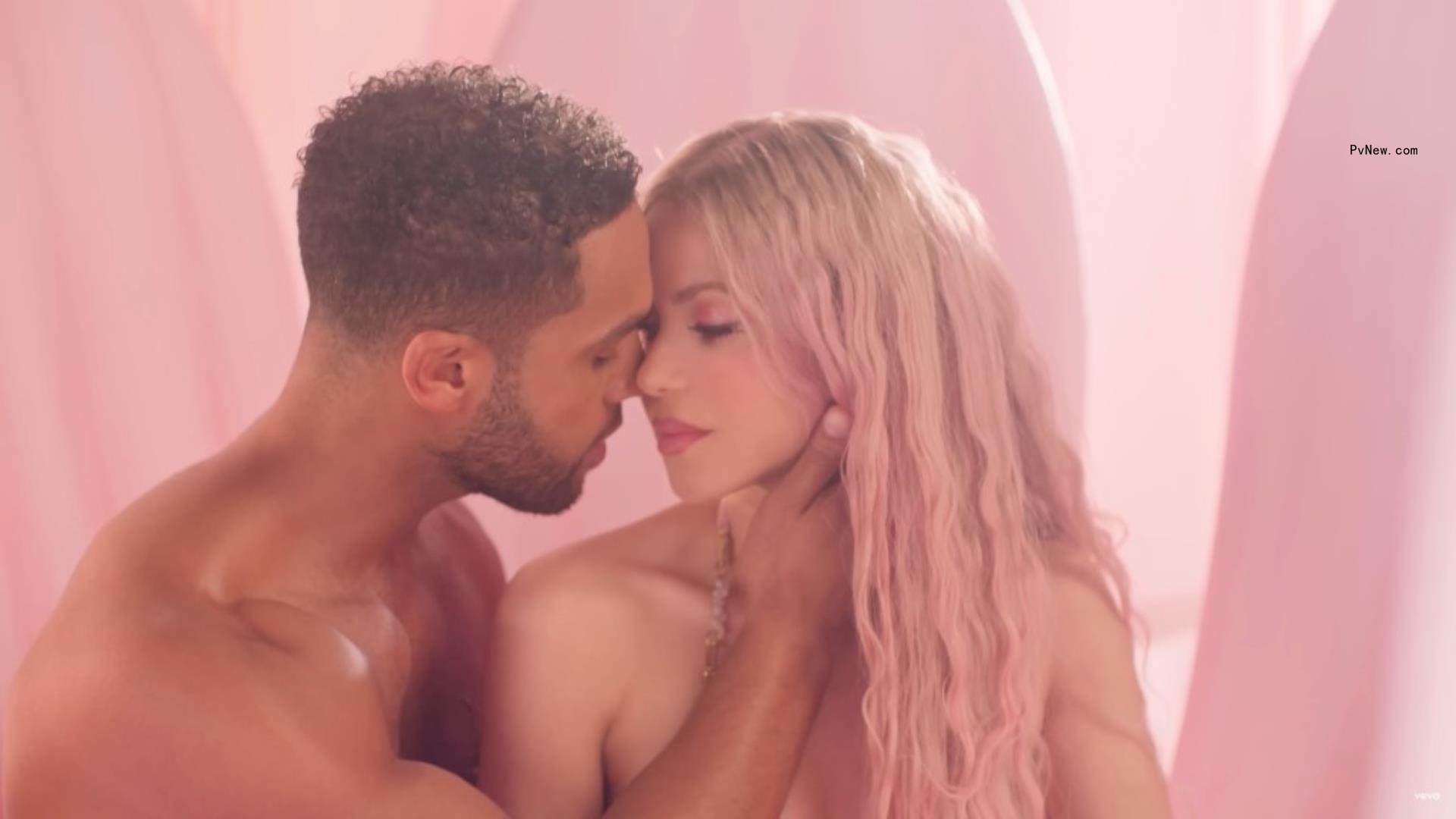 Shakira with pink hair and bare shoulders apparently kissing a topless man