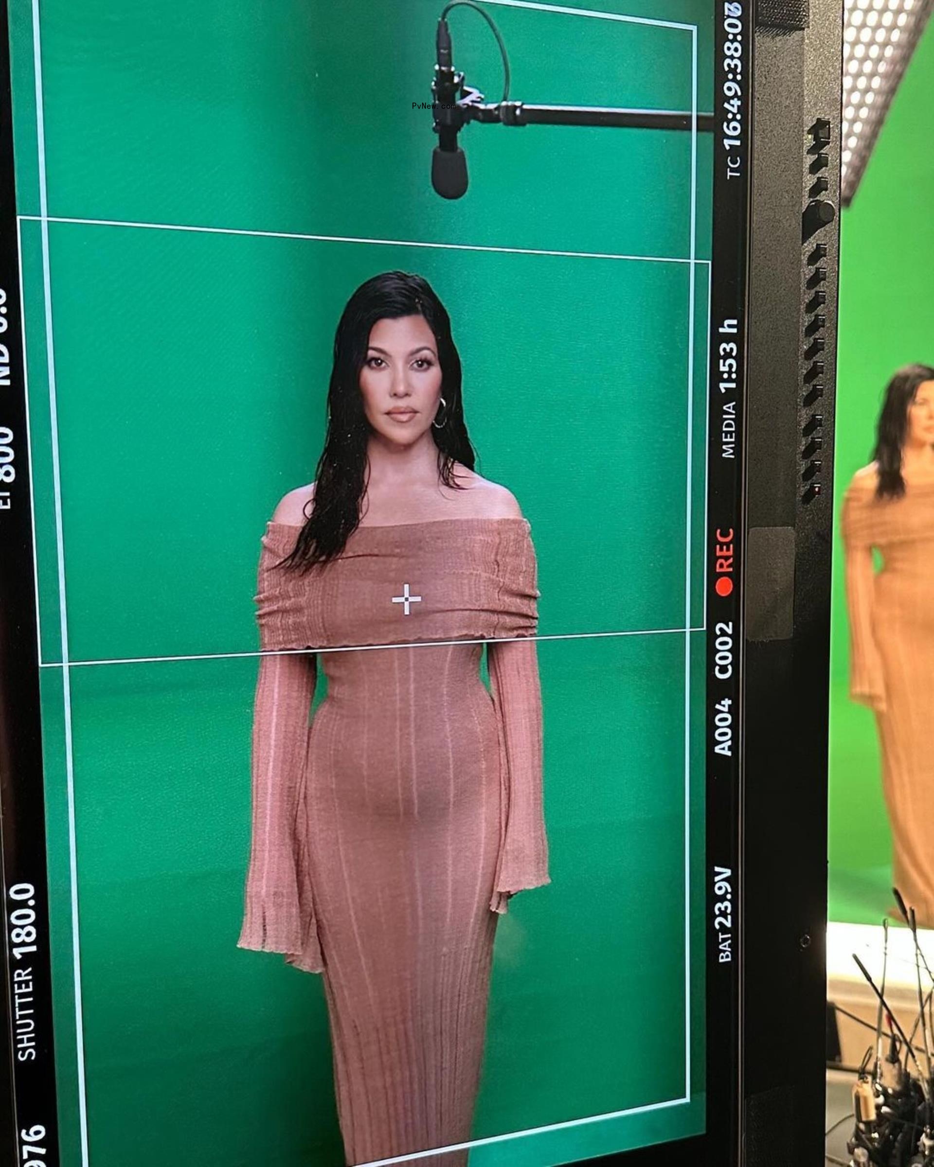 Kourtney Kardashian standing in front of a green screen.