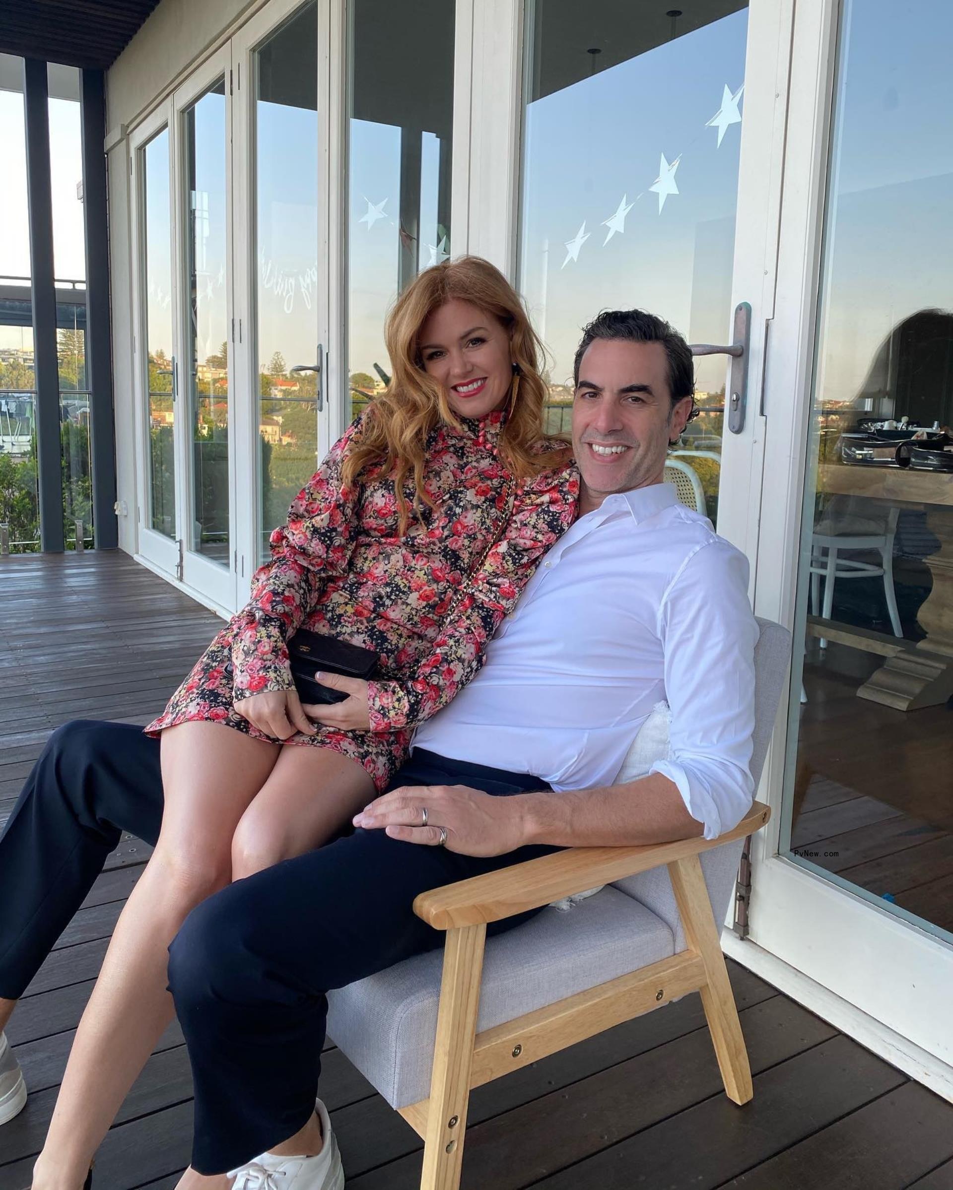 Isla Fisher sitting on Sacha Baron Cohen's lap.