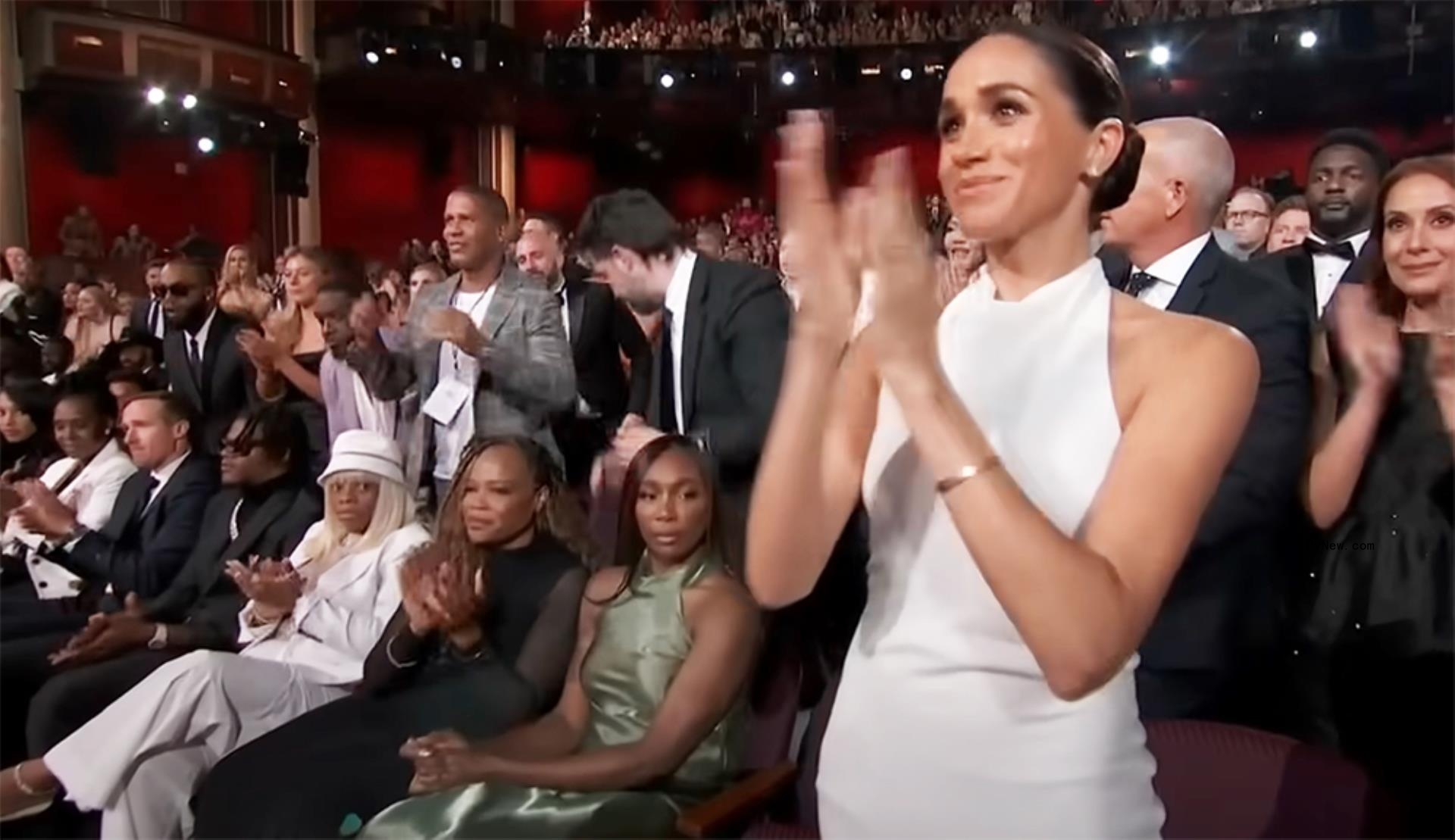 Meghan Markle clapping and standing with Venus Williams sitting next to her