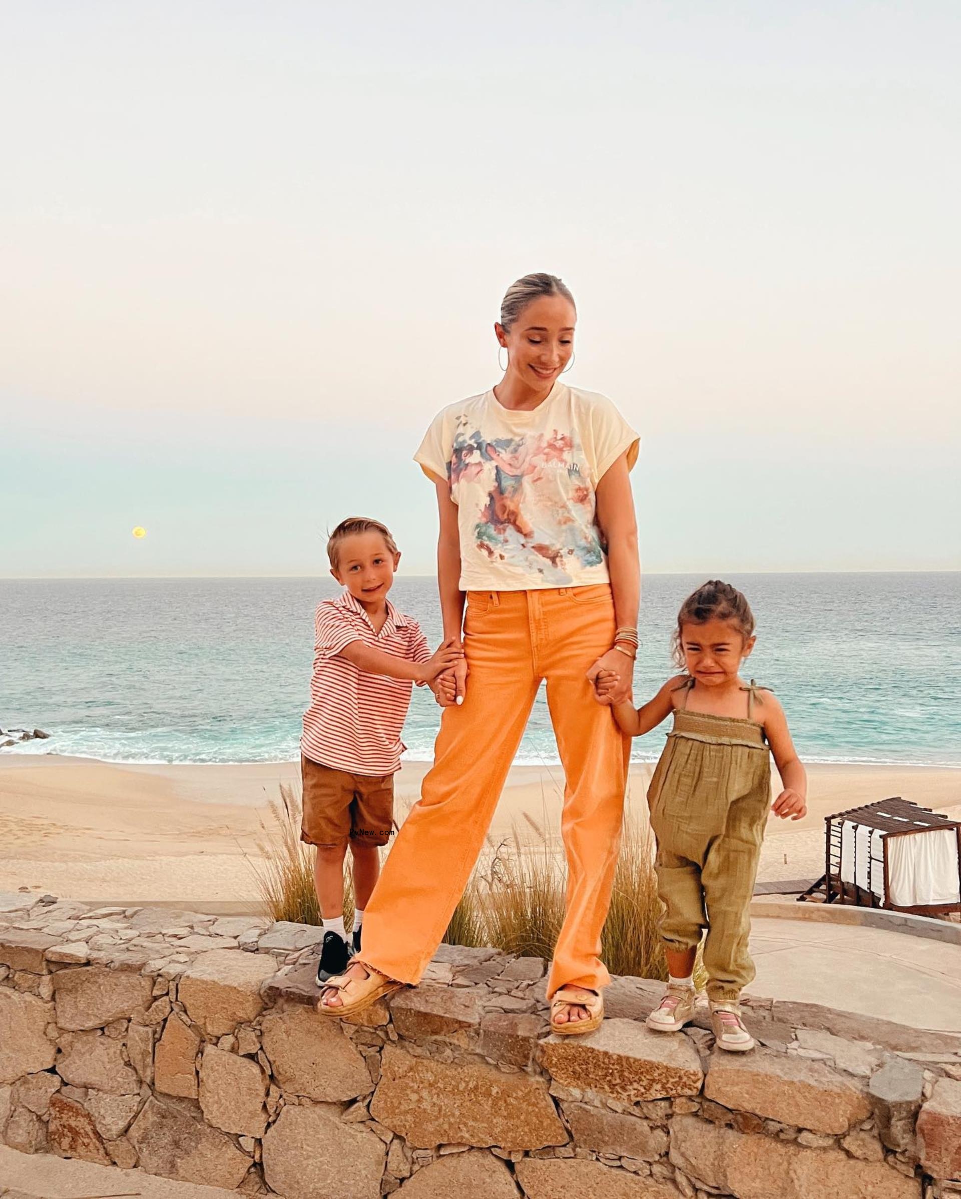 aurora culpo and her two kids standing on a stone wall at the beach