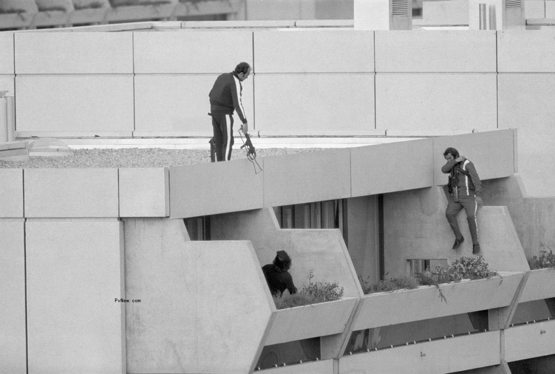A black-and-white photo of militia standing with guns over a roof