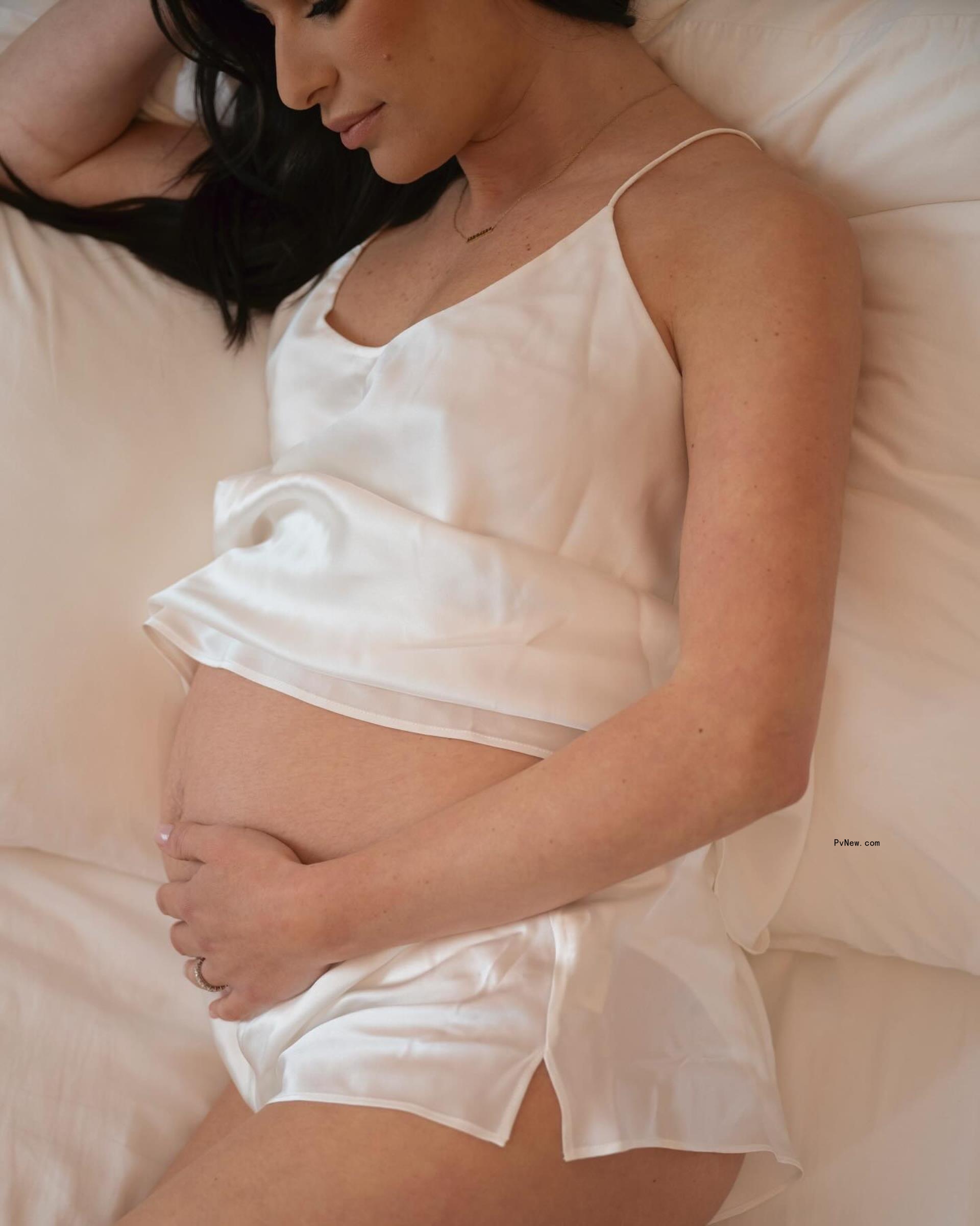 Michele cradles her baby bump in white pajamas via Instagram.