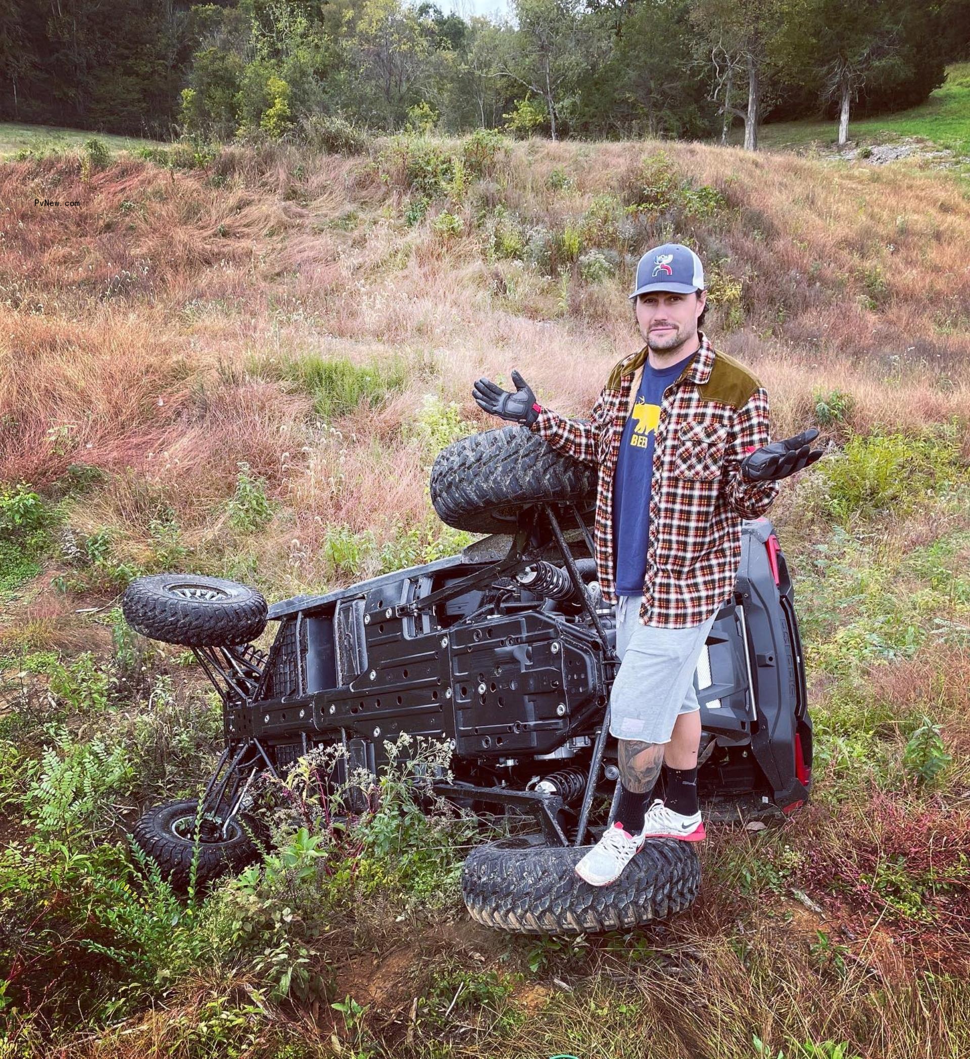 josh hall shrugging next to an overturned vehicle in a field