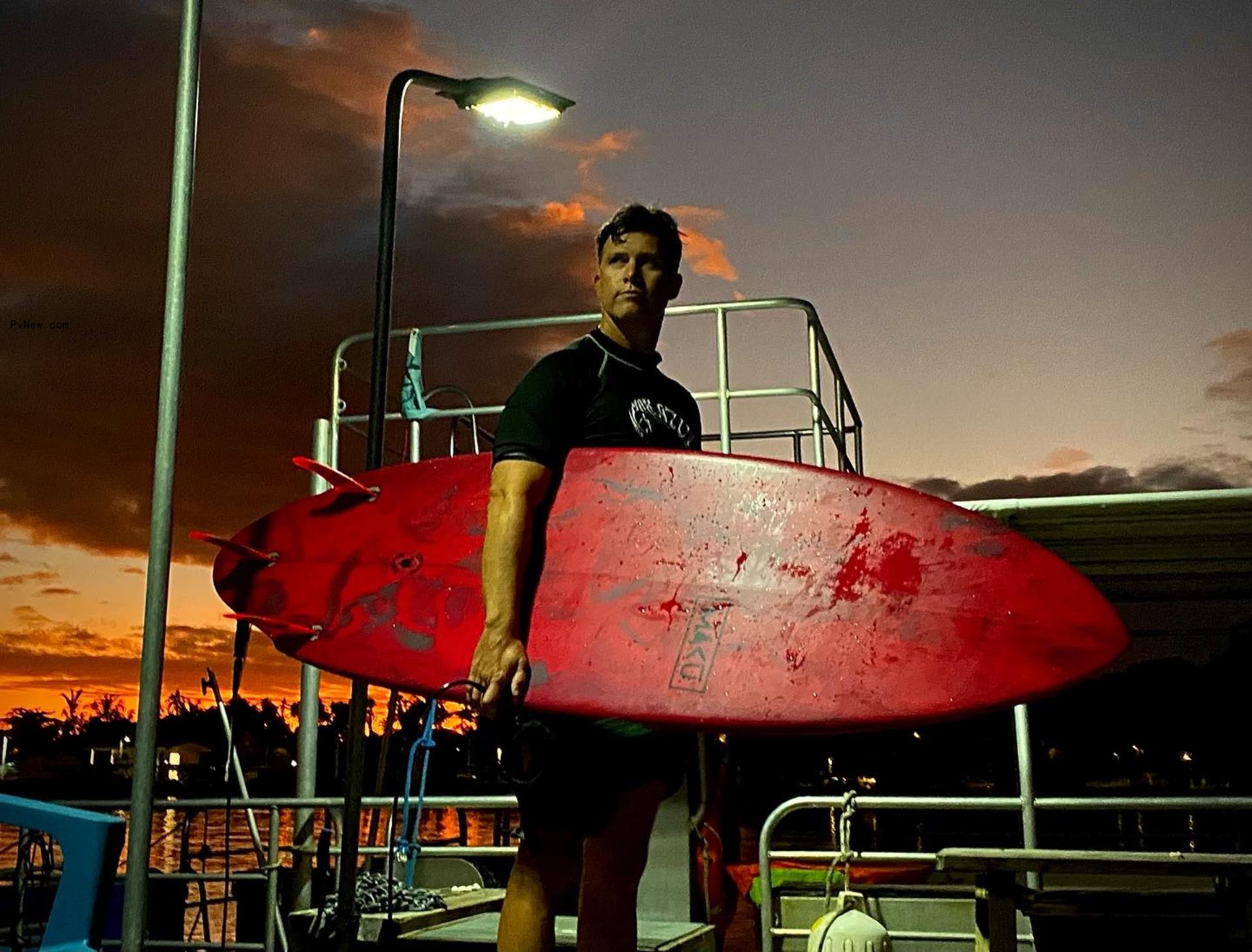 colin jost holding a surfboard 