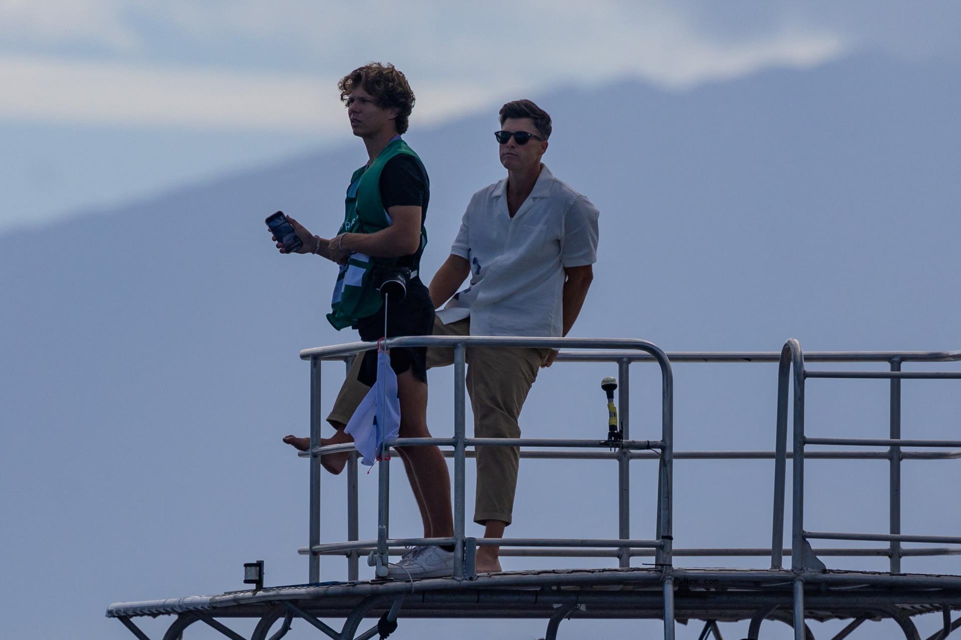 colin jost and another man sitting on a me<i></i>tal dock
