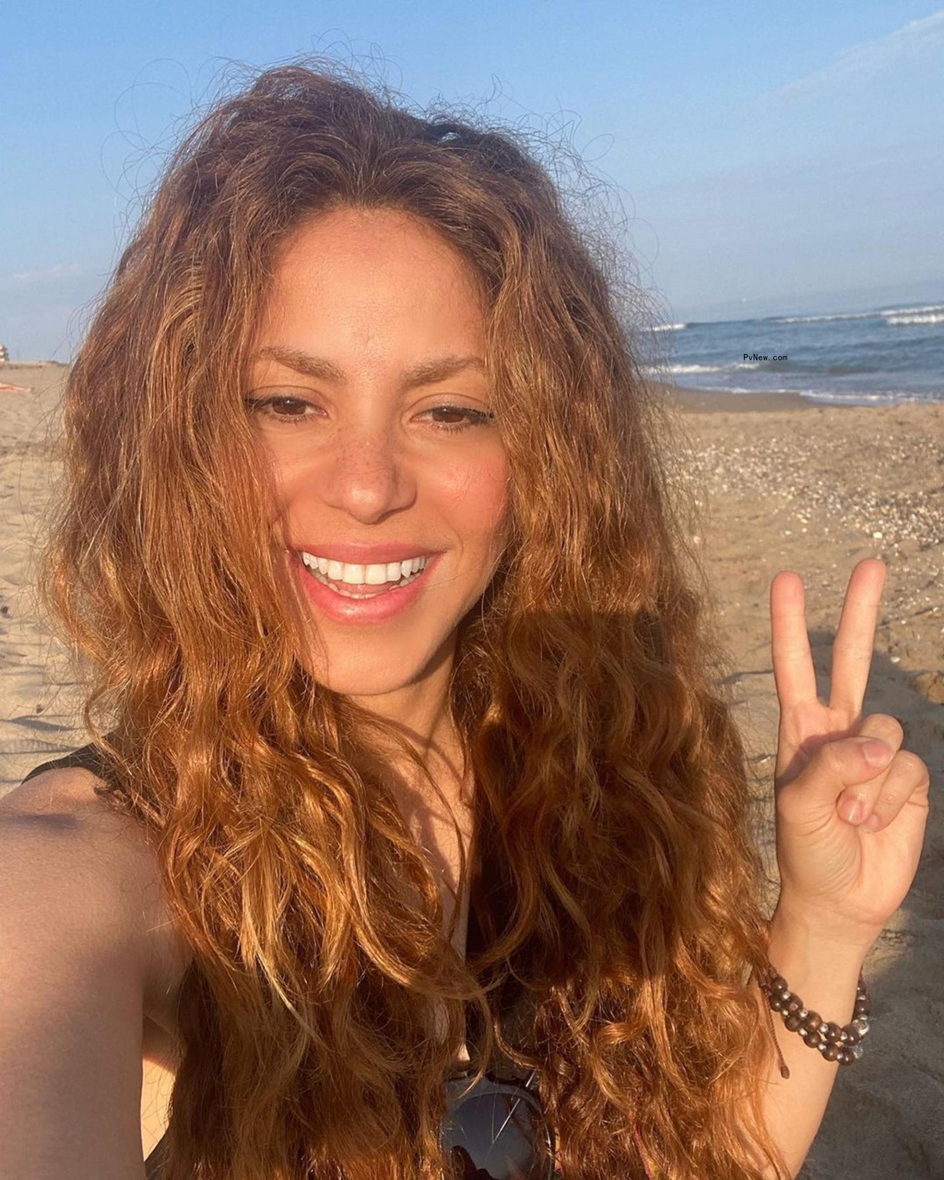 Shakira throwing up a peace sign at the beach.